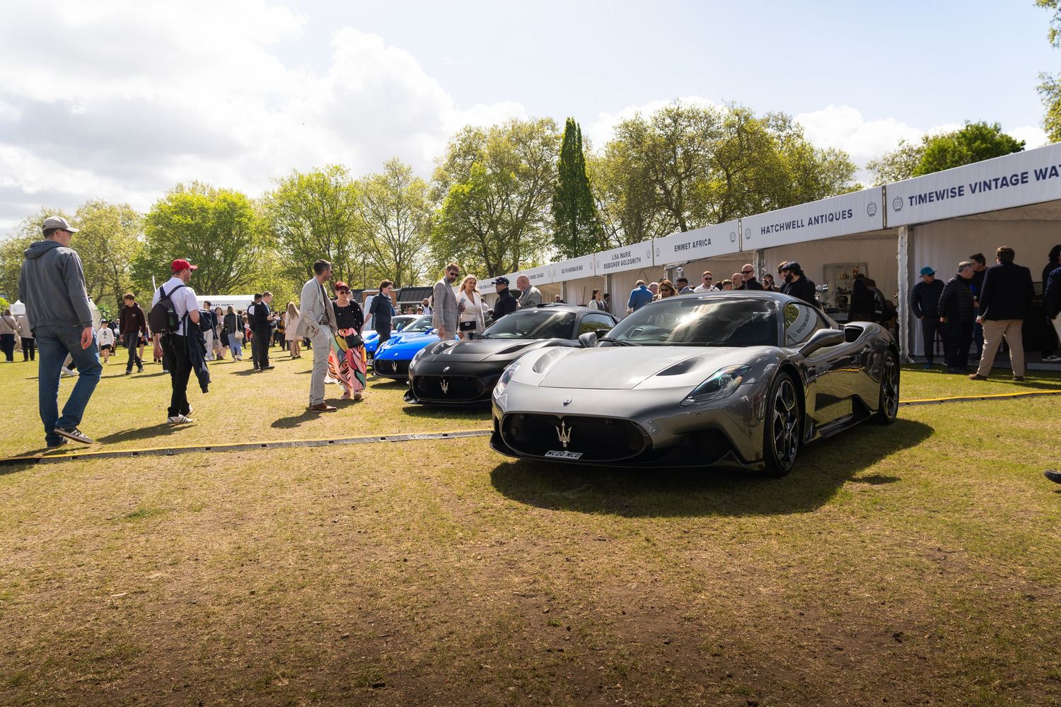 Multiple Maserati MC20 supercars on display at an outdoor luxury automotive show with crowds of spectators.