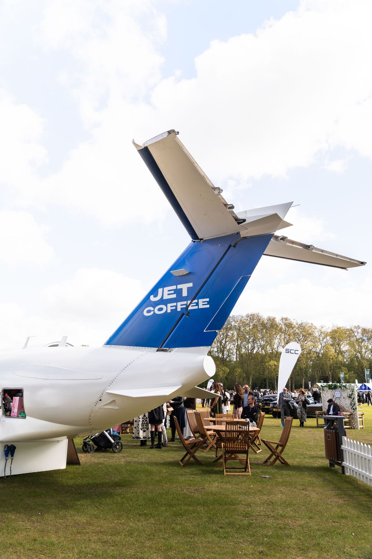 Tail section of a blue and white jet aircraft branded Jet Coffee at an outdoor event on grass.