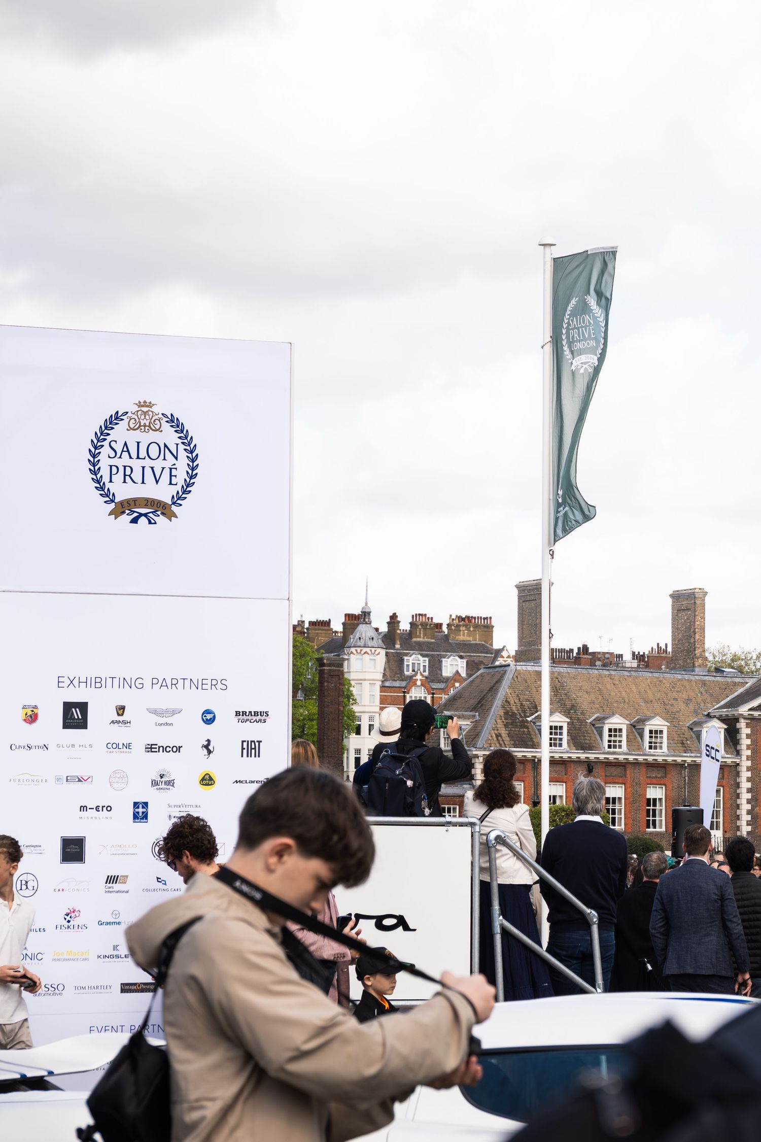 Salon Prive luxury car show signage with exhibiting partners banner and flag at event entrance.