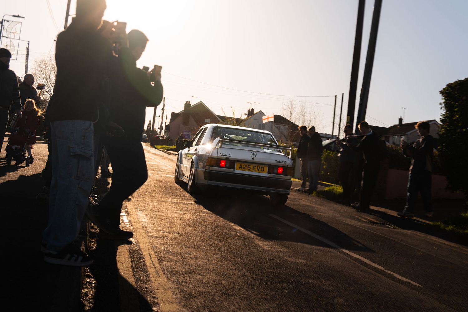 Classic silver Porsche 944 driving past spectators at a sunny car meet event.