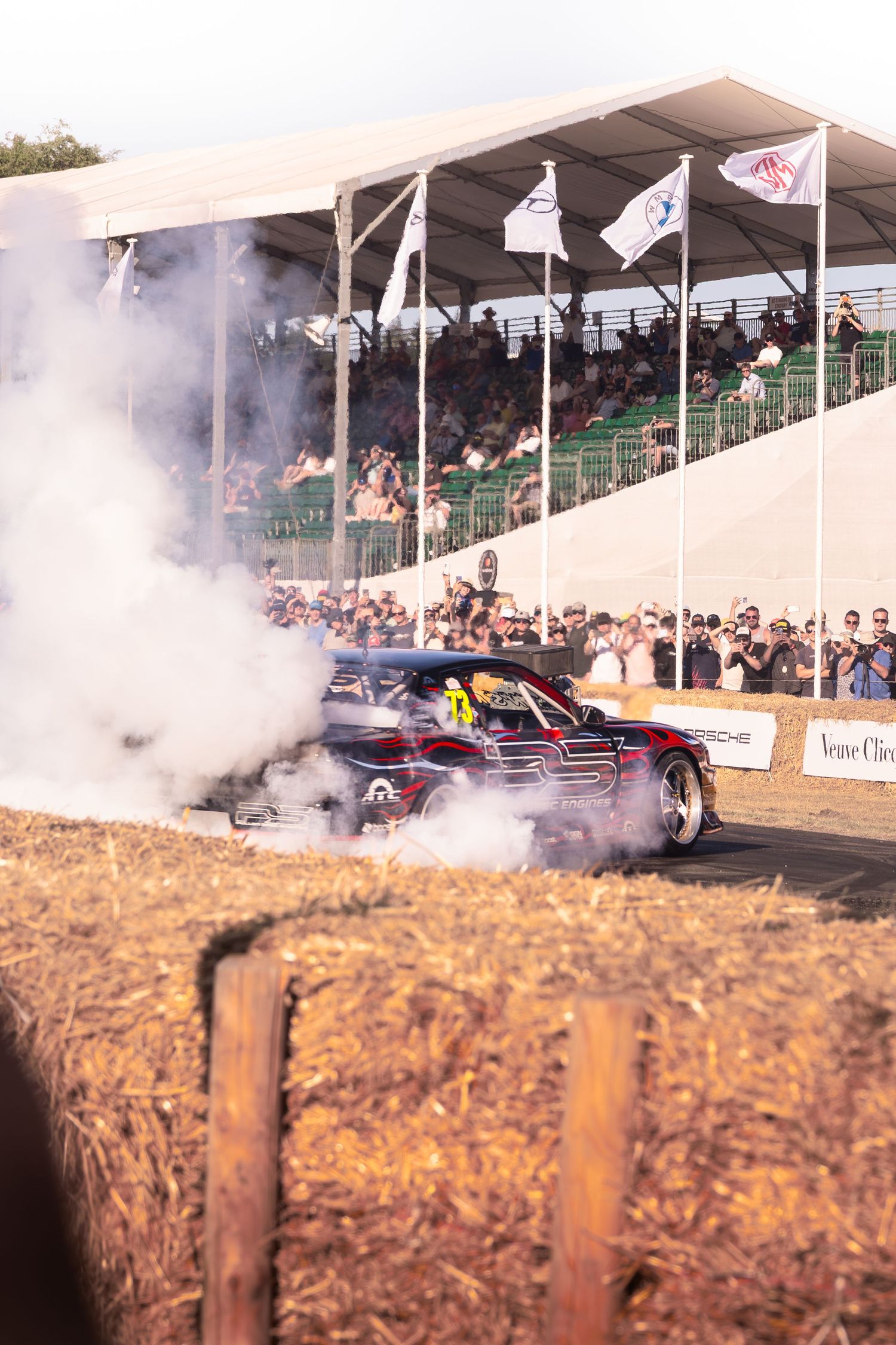 A racing car performs a dramatic burnout at Goodwood Festival of Speed, surrounded by smoke and cheering spectators.