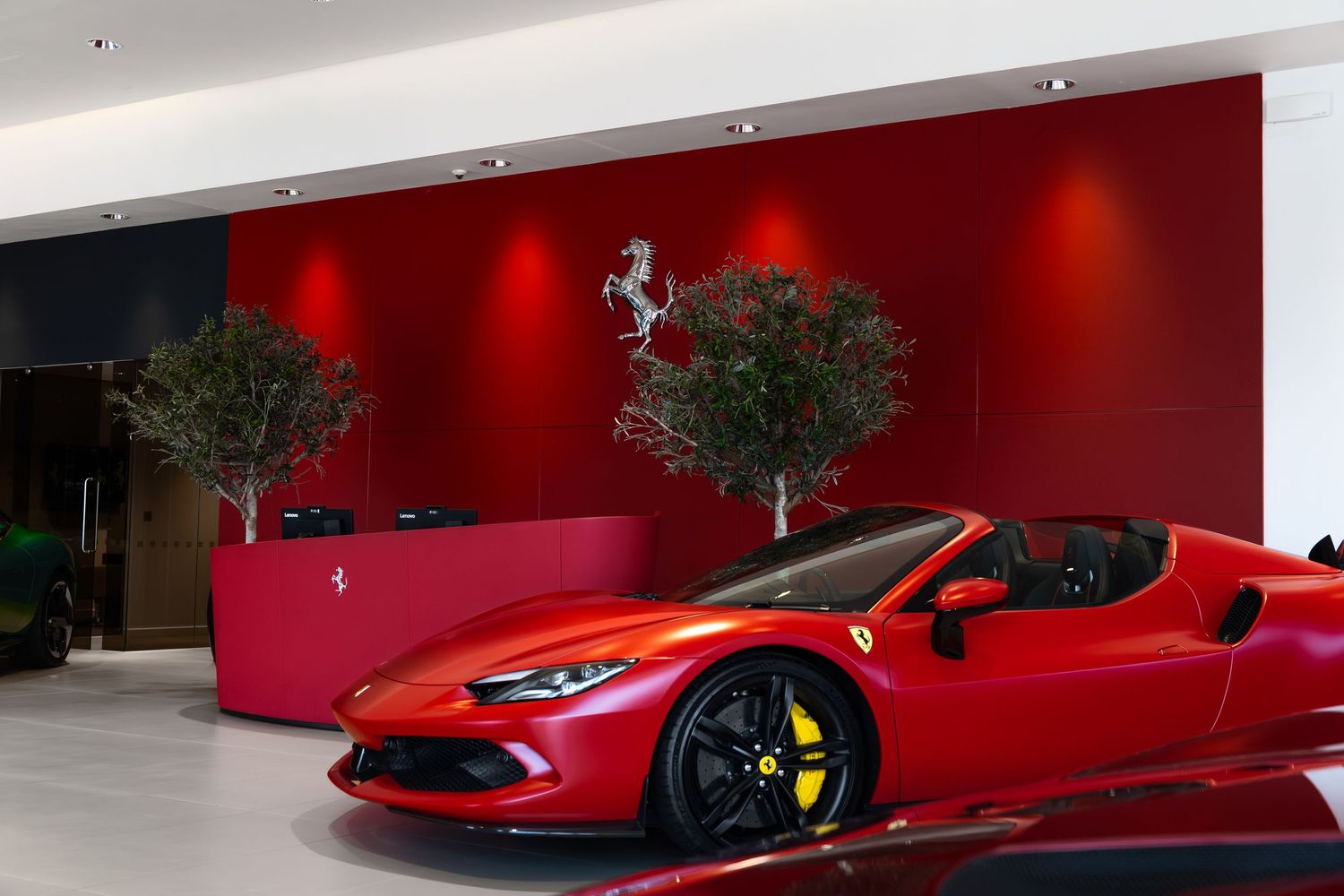 Red Ferrari sports car displayed in a luxury Ferrari dealership showroom with red walls and decorative trees.