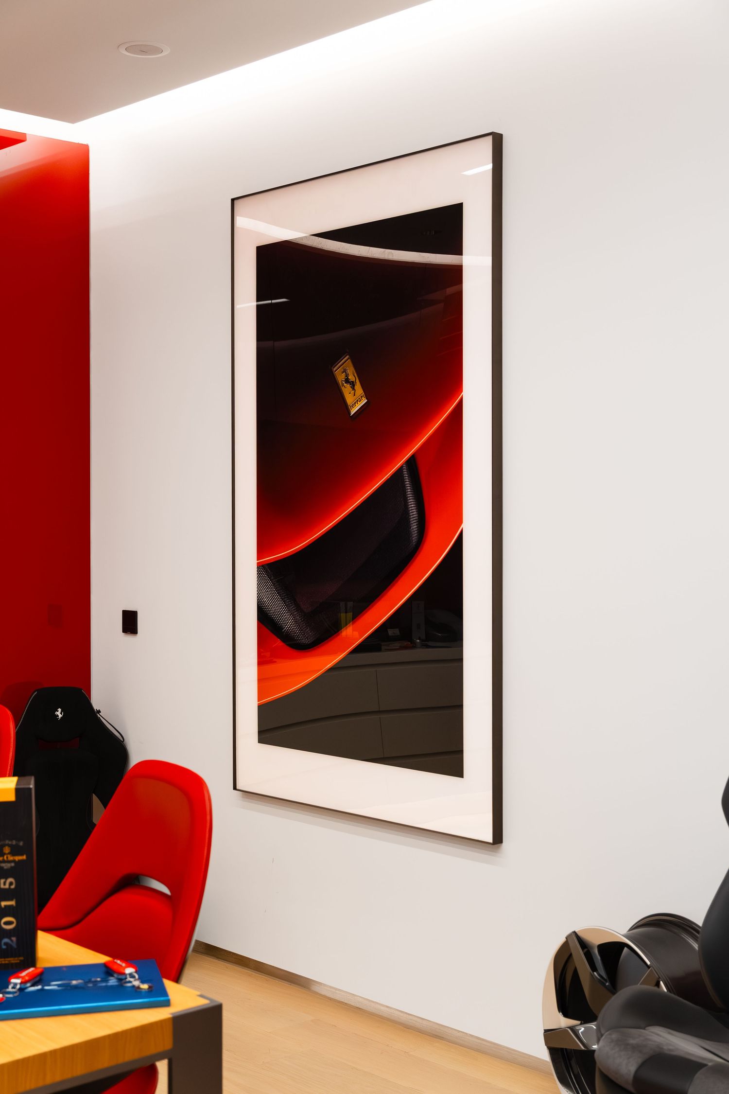 Large framed Ferrari close-up photograph on white wall in modern showroom with red accents and wooden flooring.
