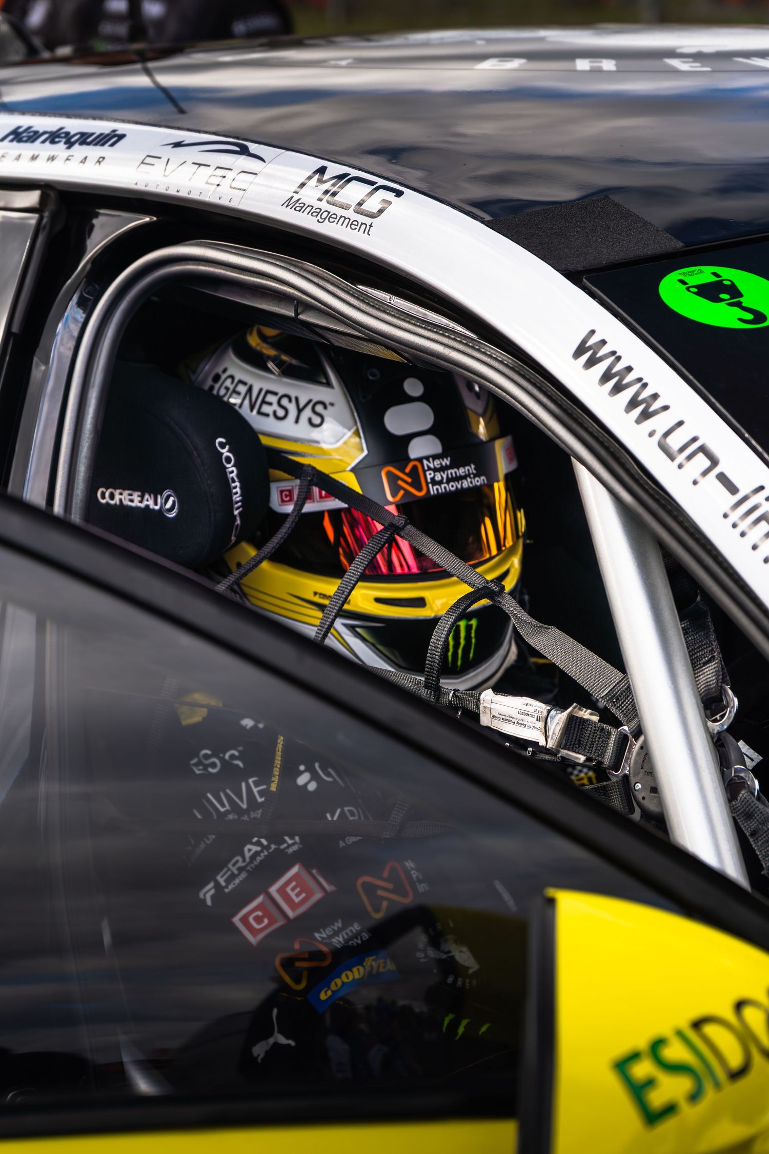 BTCC racing driver wearing Monster Energy helmet seated inside roll cage race car cockpit.