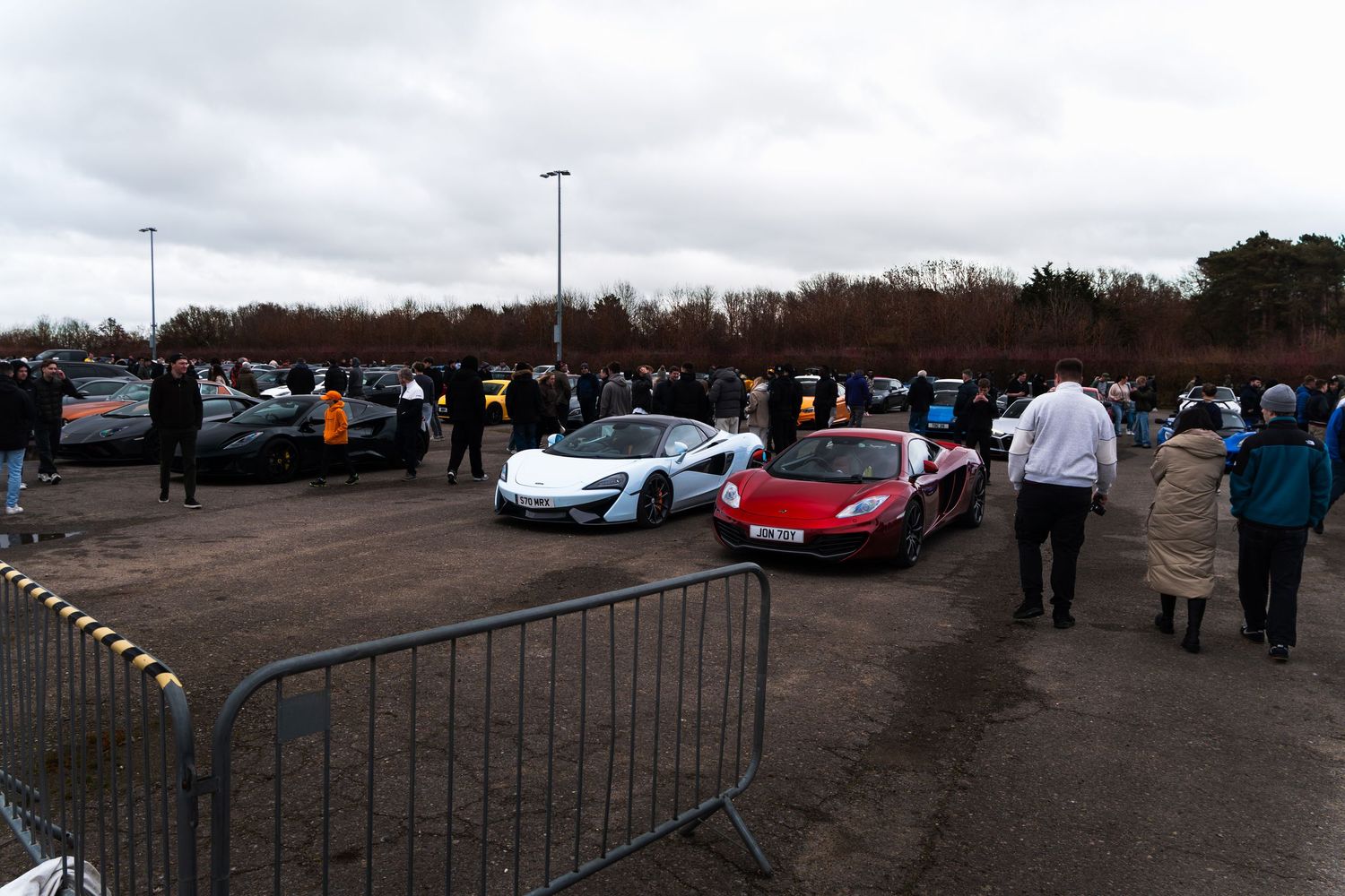 Crowd of car enthusiasts viewing supercars including McLaren and Ferrari at a UK meet.
