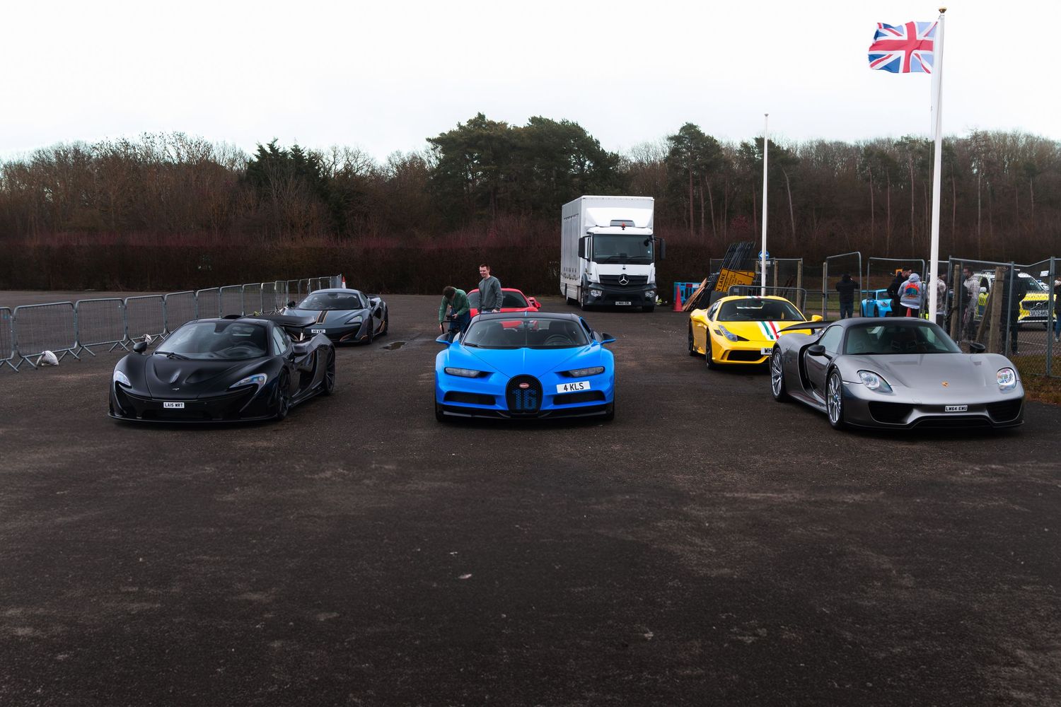 Rare supercars including Bugatti Chiron, McLaren Senna and Porsche lined up at UK track day with Union Jack flag.