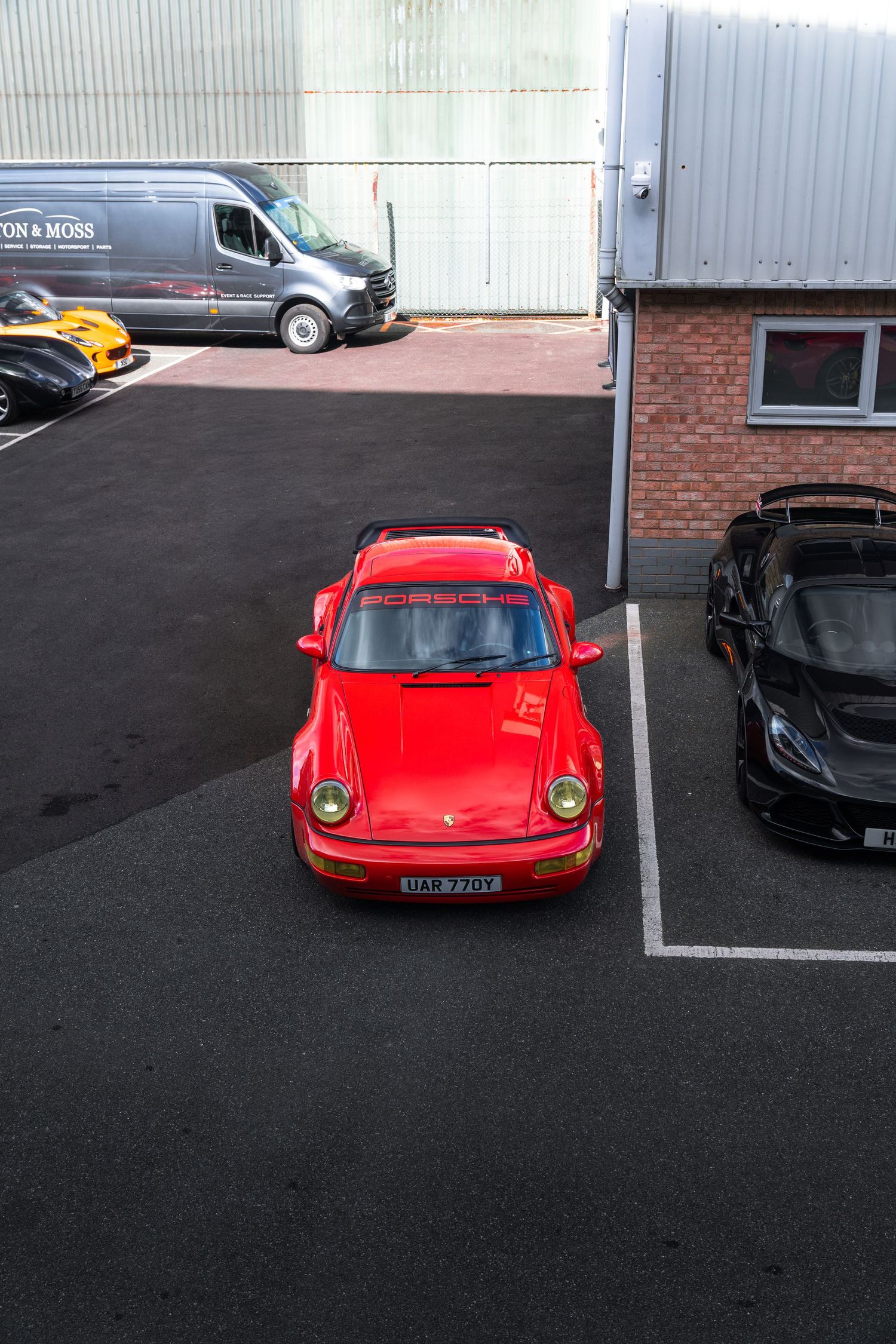 Red Porsche 911 964 viewed from above in a car dealership parking lot.