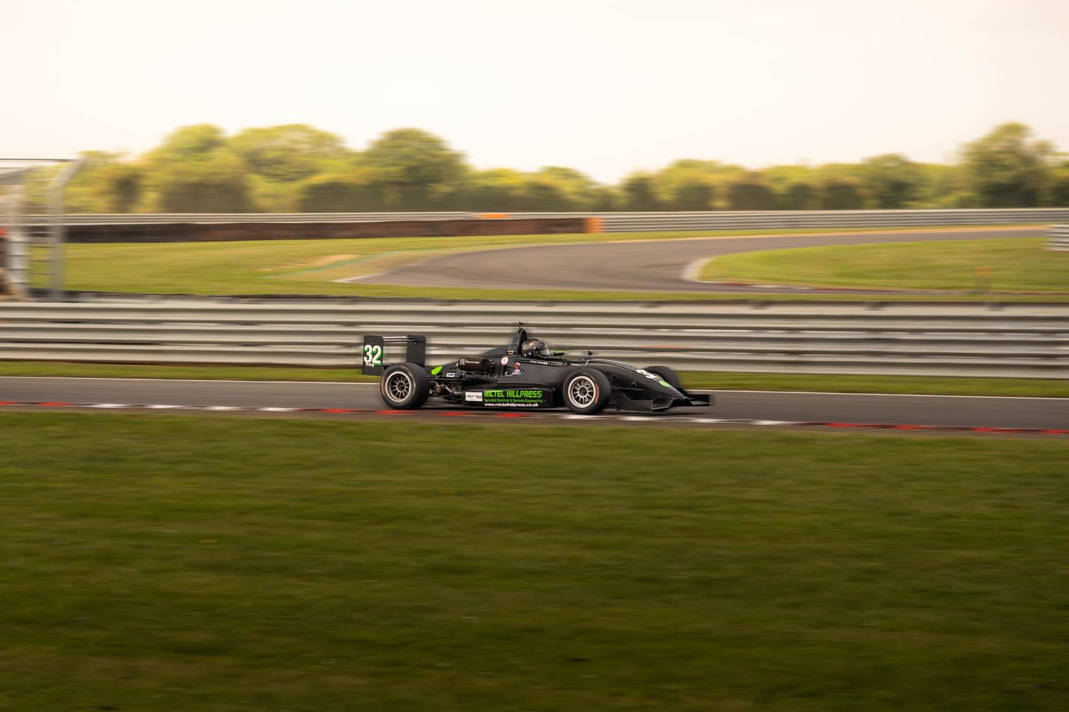 Black formula racing car speeding along a race circuit at dusk.