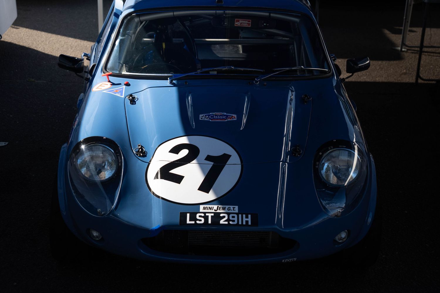 Blue classic racing car number 21 with license plate LST 29IH parked in paddock.