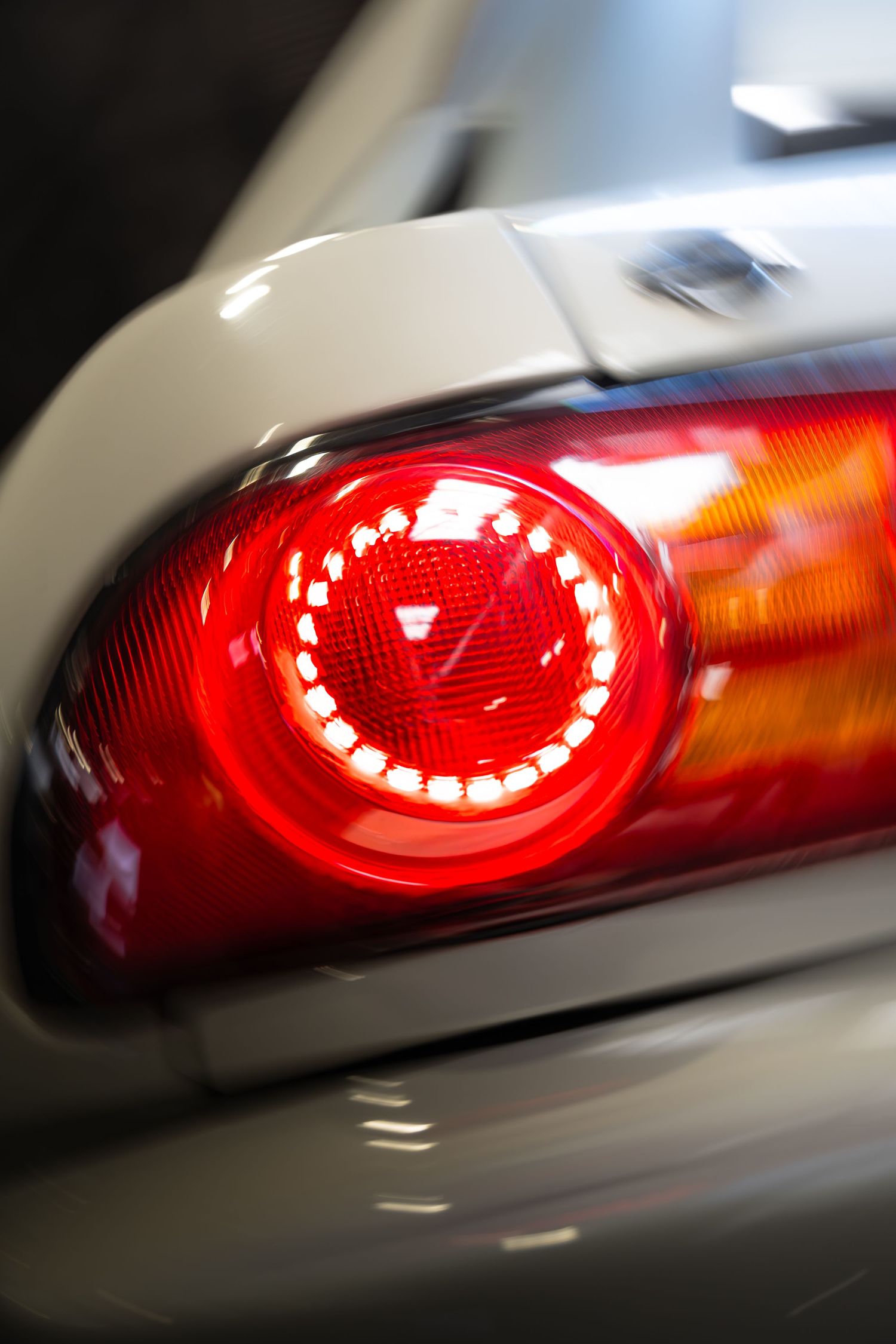 Close-up of a circular red LED tail light on a silver sports car.