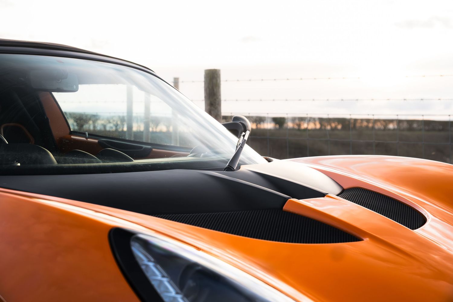Detail shot of orange Lotus Elise hood scoop and windscreen against bright coastal background.