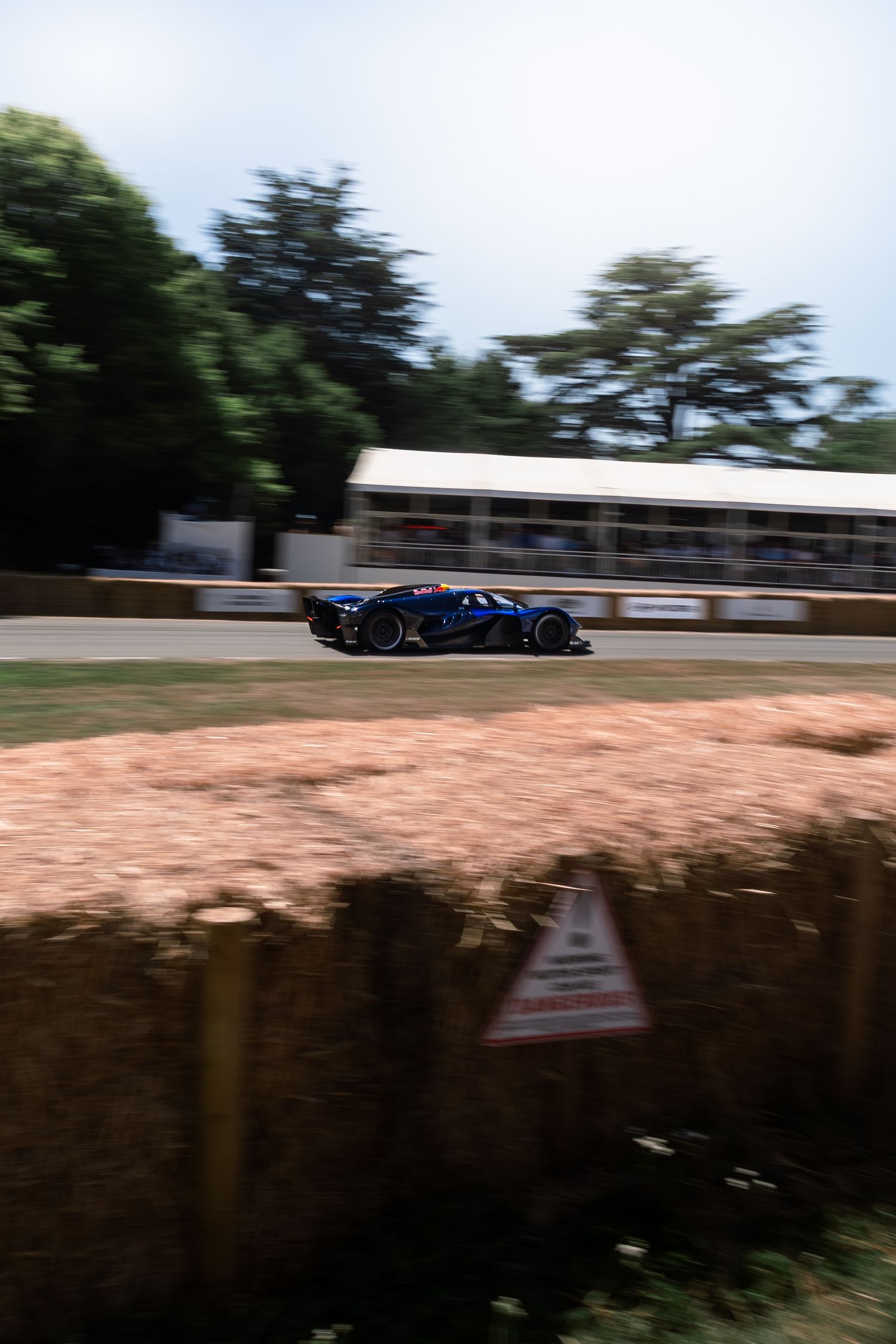 A blue racing car speeds past hay bales at the Goodwood Festival of Speed hillclimb event.