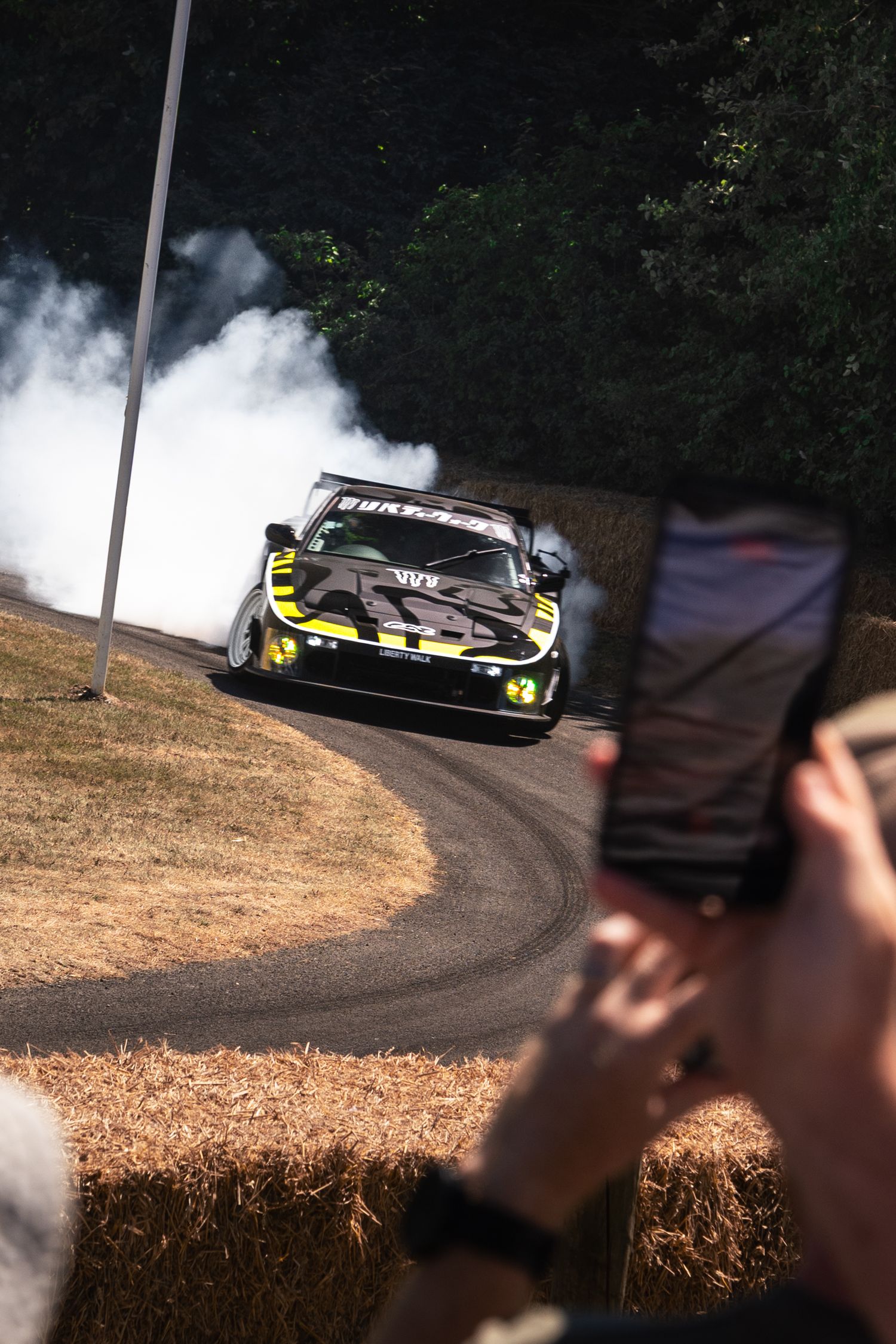 Black and yellow race car drifting with smoke at Goodwood Festival of Speed hillclimb event.