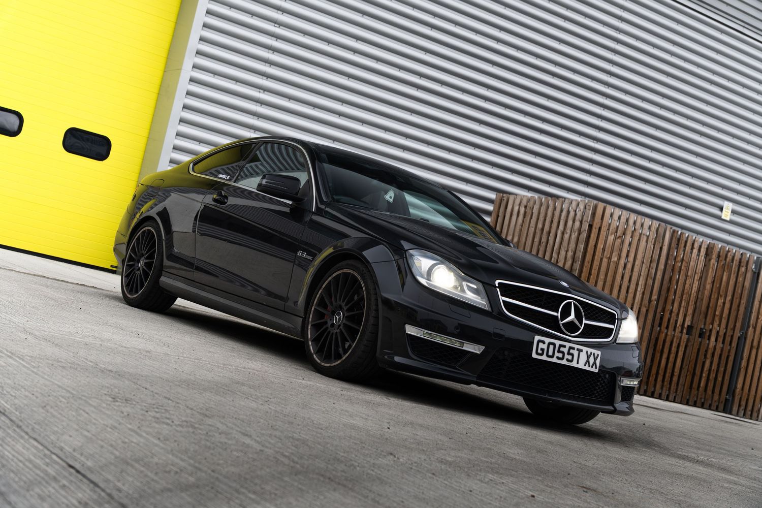Black Mercedes-AMG C63 coupe parked at an angle near yellow garage doors and wooden panel wall.