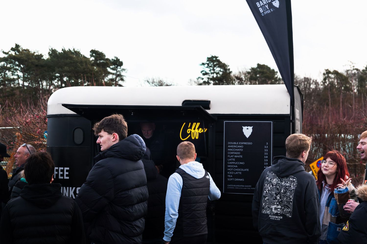 People queuing at a black coffee van trailer at an outdoor car meet event in the UK.