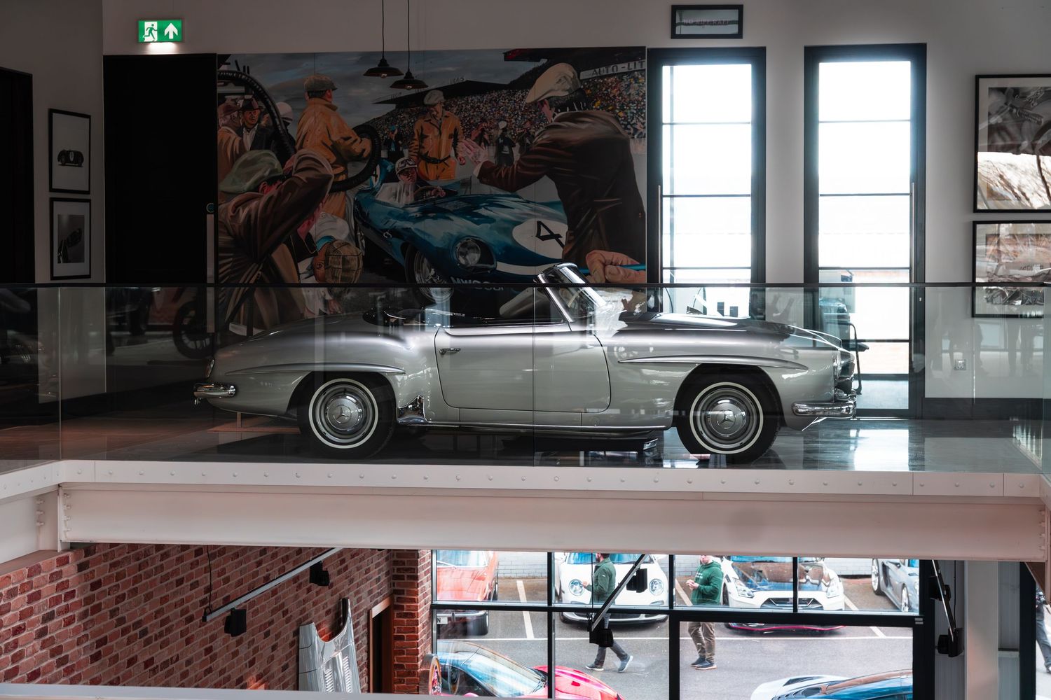 Silver vintage Mercedes-Benz 190SL convertible displayed on elevated platform in modern gallery space.