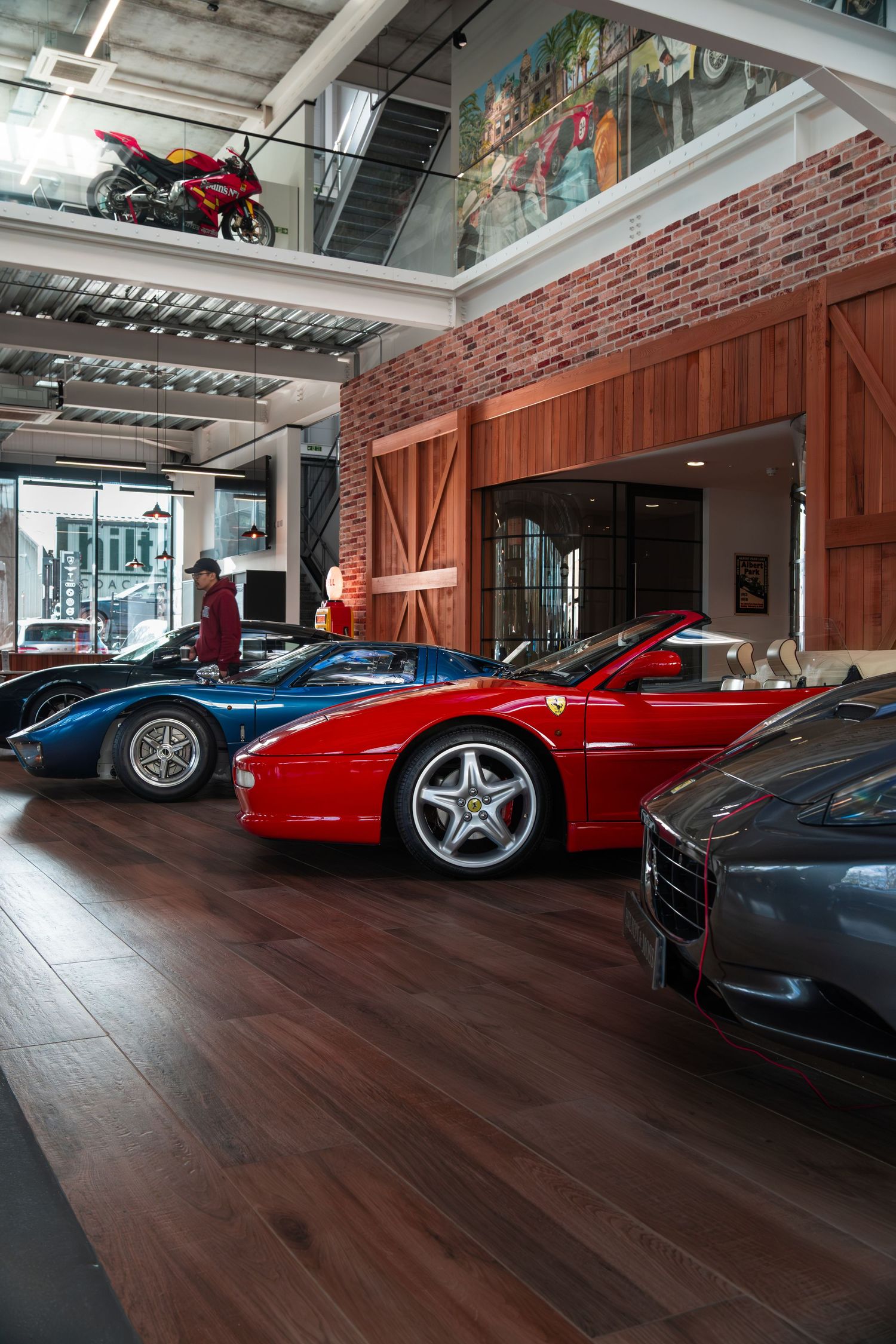 Luxury car showroom featuring a red Ferrari 355 Spider and blue supercar on polished hardwood floors.