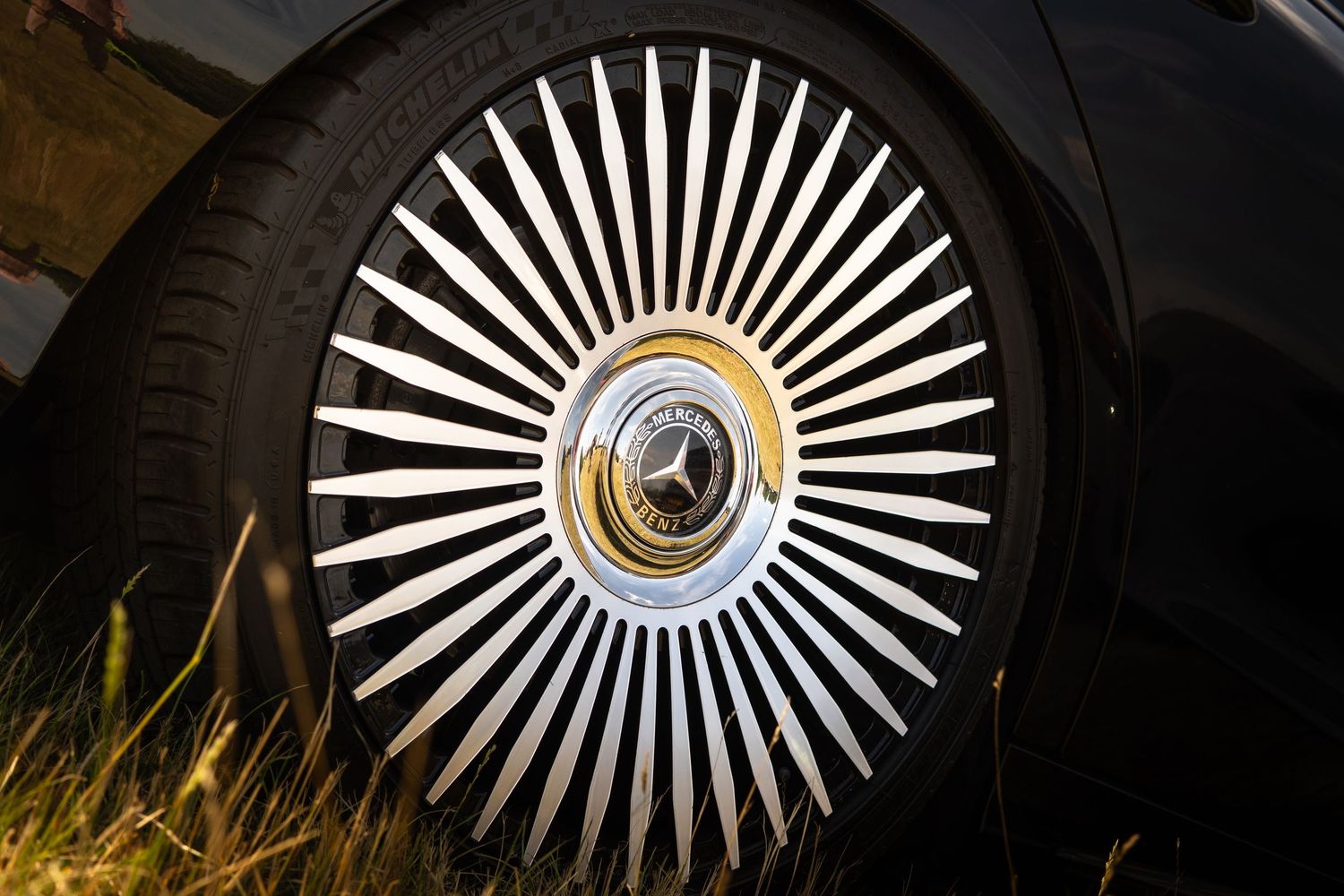 Ornate Mercedes-Benz spoke alloy wheel with gold center cap on a black luxury car.