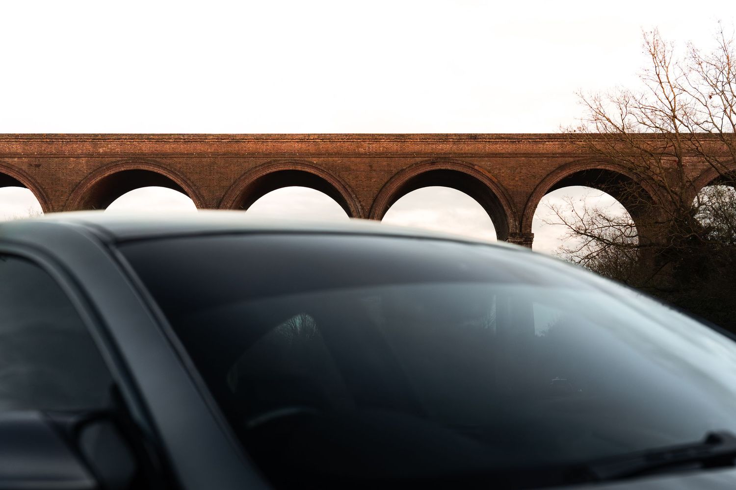 BMW M3 rooftop view with brick arched viaduct visible in background against cloudy sky.