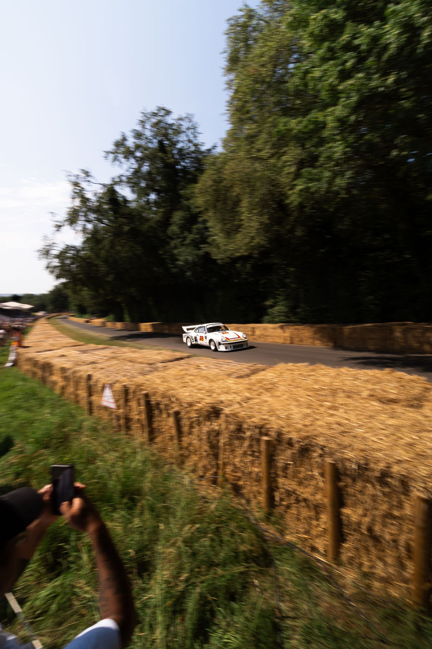 White rally car navigating a hay bale lined track at Goodwood Festival of Speed, surrounded by lush green trees.