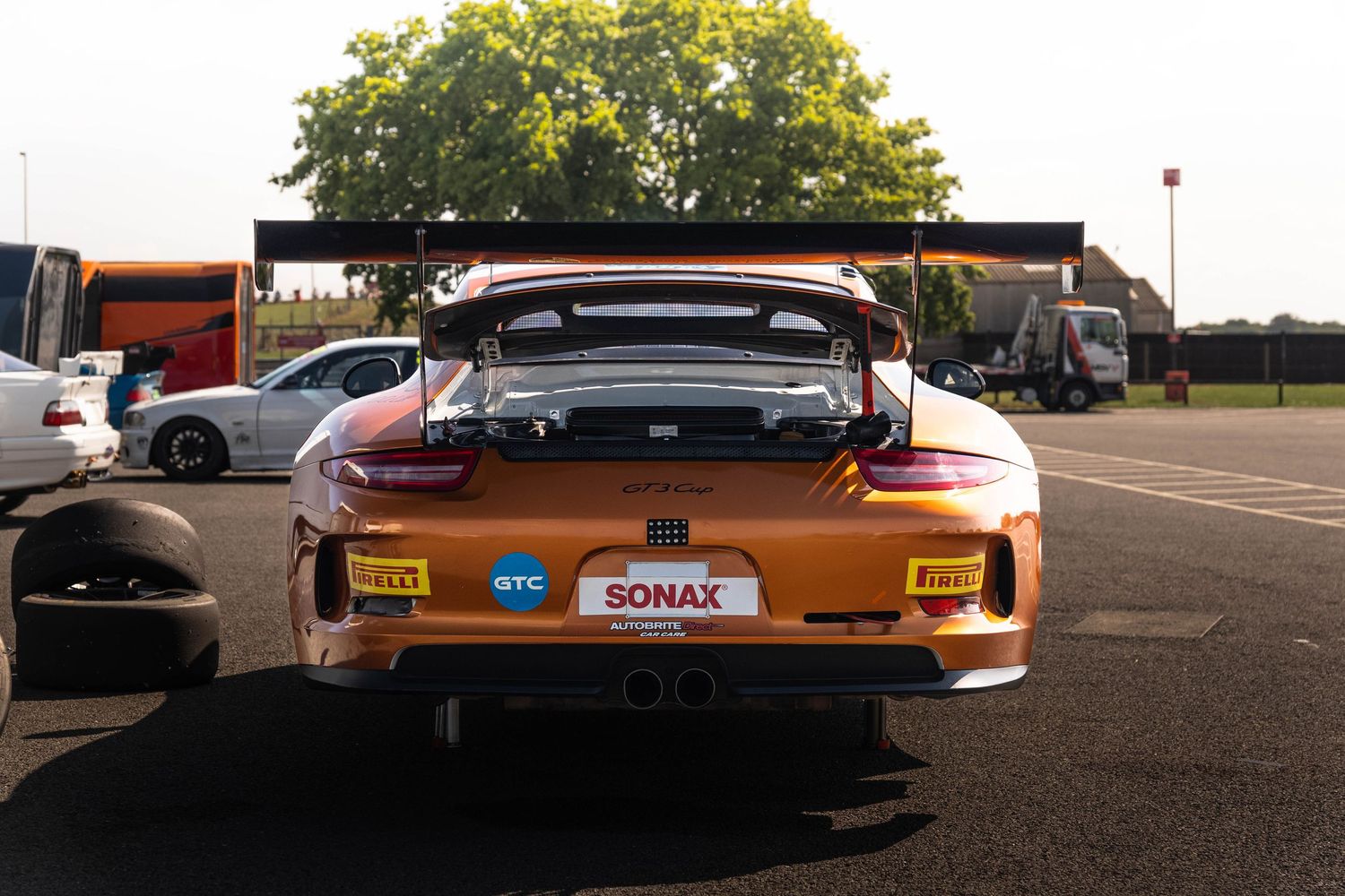 Rear view of an orange Porsche 911 GT3 race car with SONAX and GTC sponsorship in paddock.