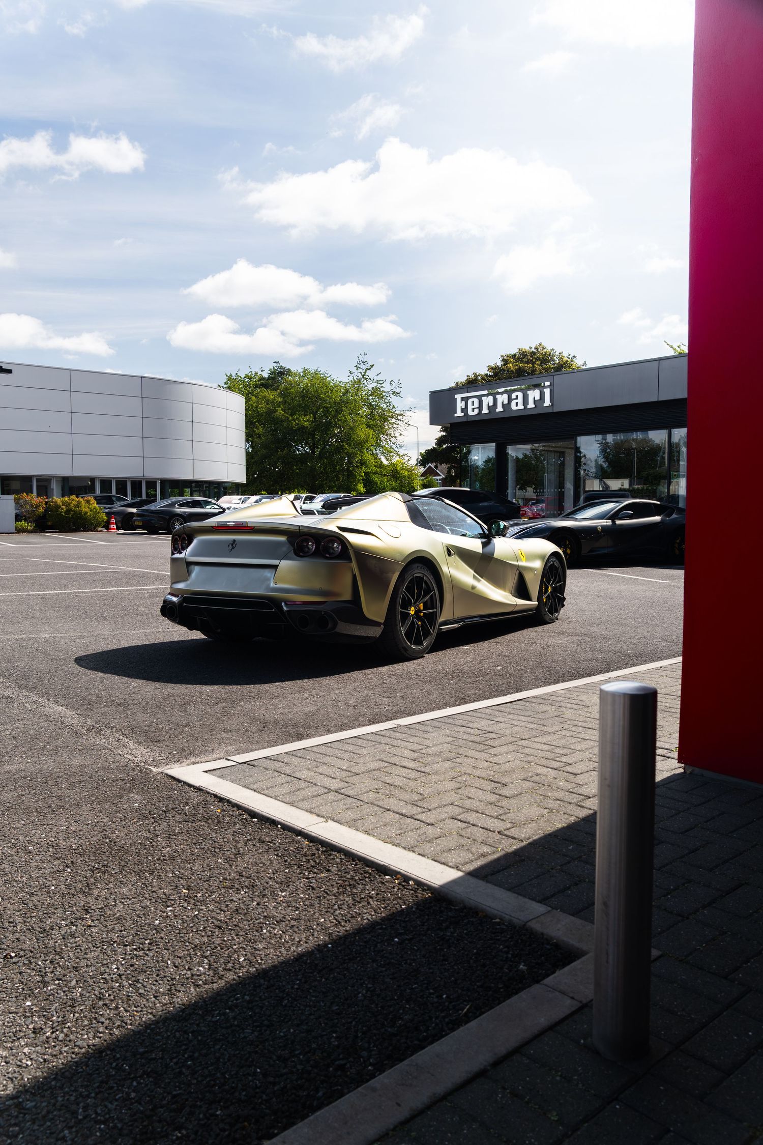 Gold Ferrari sports car parked outside a Ferrari dealership on a sunny day.