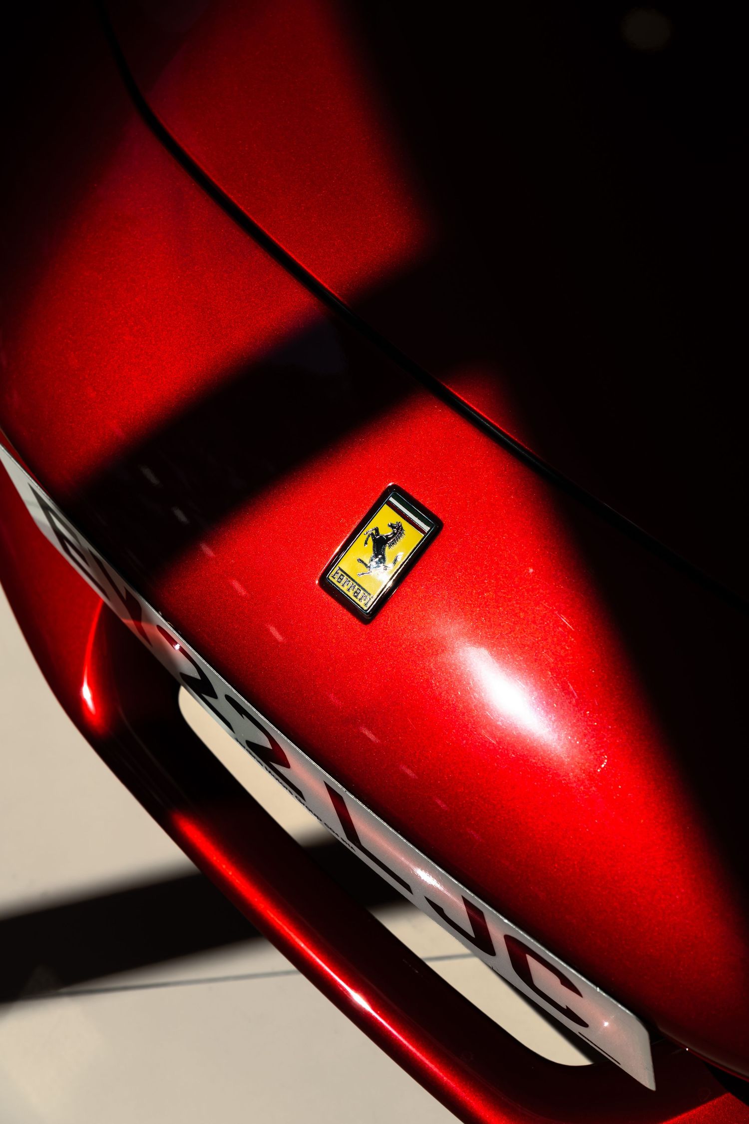 Close-up of a red Ferrari car hood featuring the iconic black prancing horse logo badge on a glossy metallic surface.