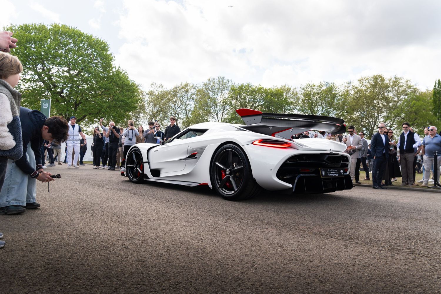 White Koenigsegg hypercar with large rear wing displayed at an outdoor exotic car show.