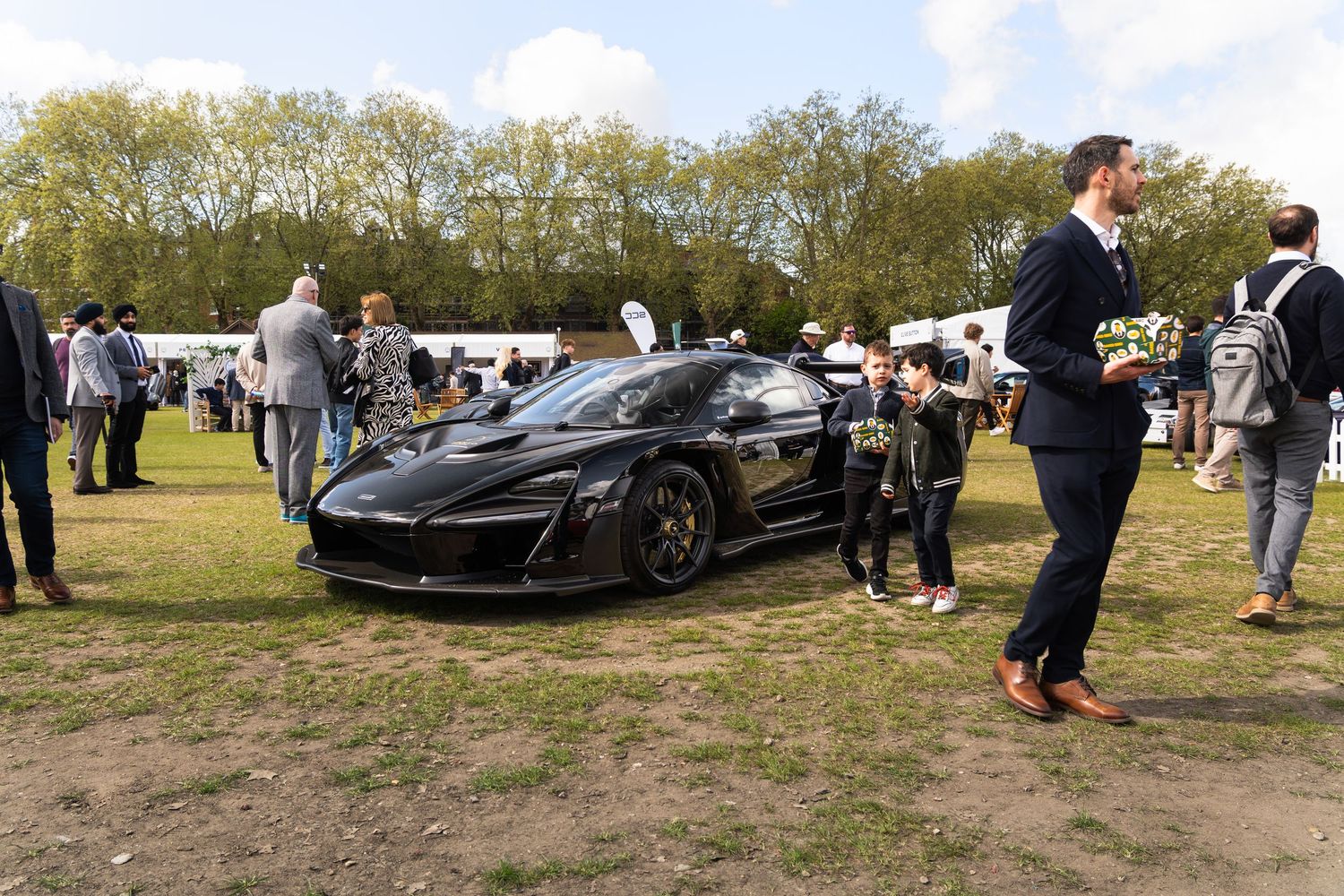 Black McLaren supercar on display at an outdoor automotive show with spectators gathered around.
