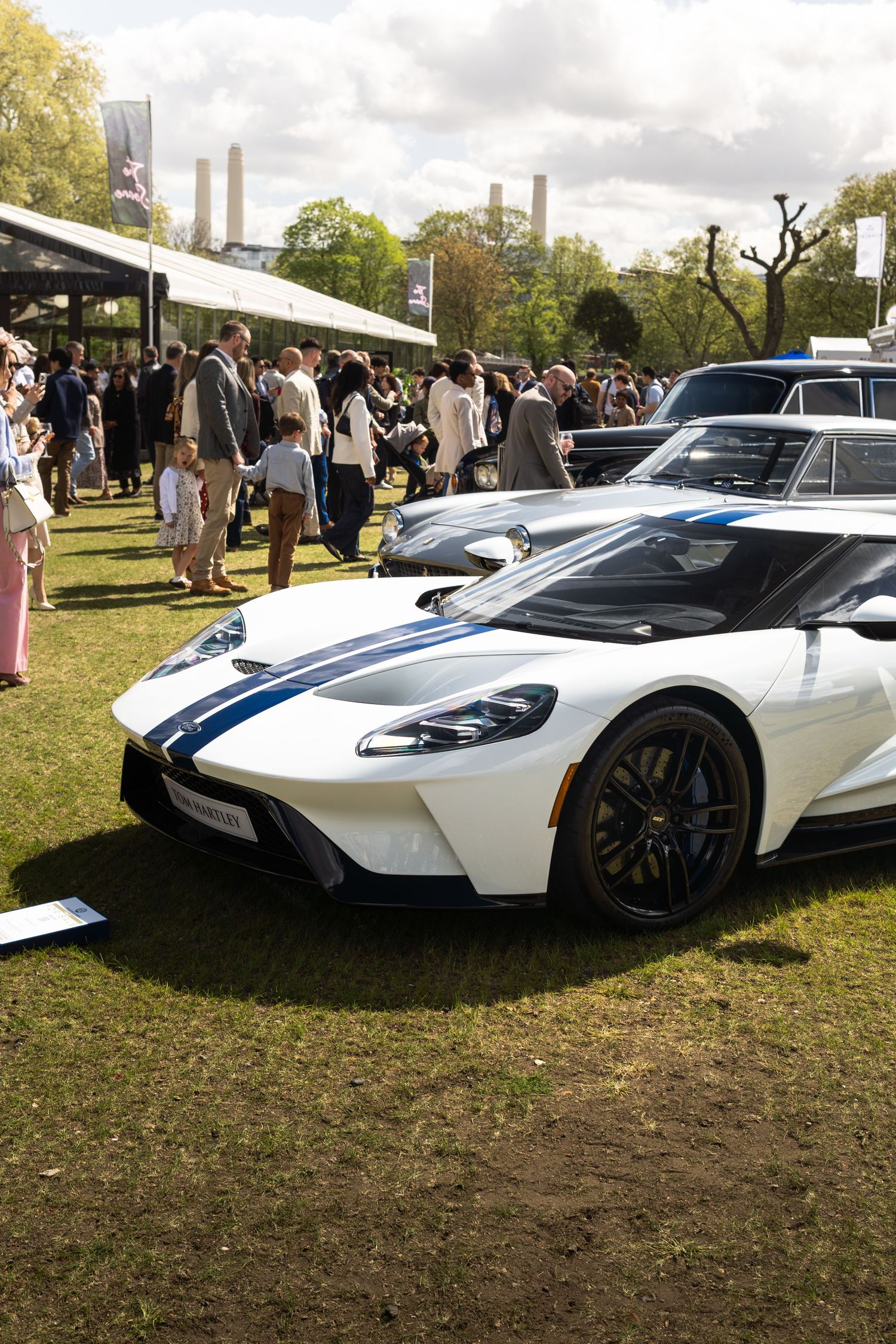 White Ford GT supercar with blue racing stripes on display at an outdoor automotive show on a sunny day.