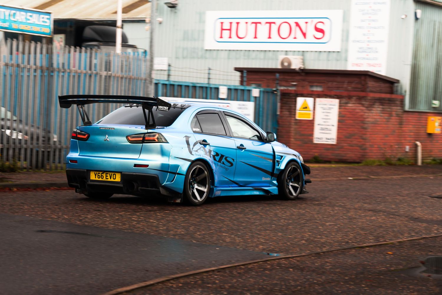 Blue widebody Mitsubishi Lancer Evolution with large rear wing parked near Huttons building.