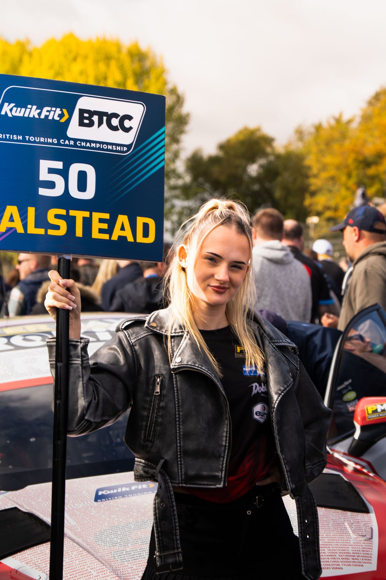 A grid girl holds a BTCC KwikFit number 50 Halstead sign at a British Touring Car Championship event.
