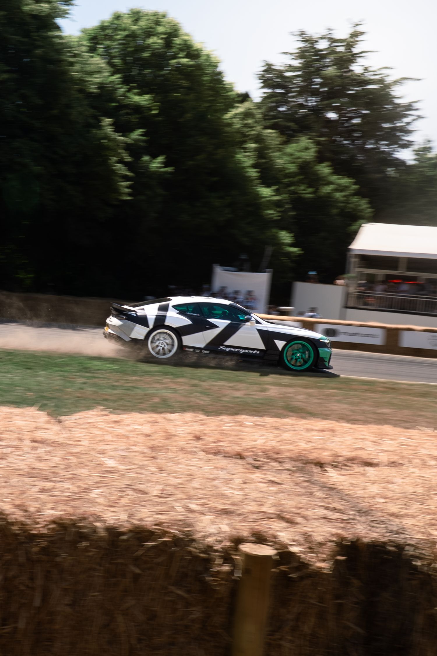 A black and white race car speeds past hay bales at the Goodwood Festival of Speed hillclimb event.