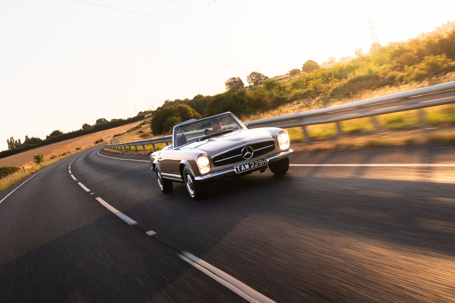 Vintage Mercedes-Benz convertible driving on a scenic road at golden hour sunset.