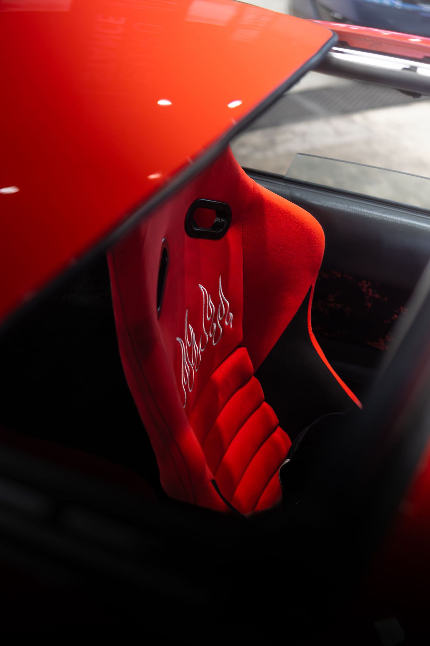 Red racing bucket seat with embroidered script logo inside a custom sports car.