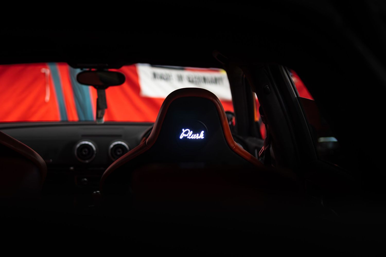 Dark interior view of a sports car featuring illuminated Recaro bucket seats with red accents.