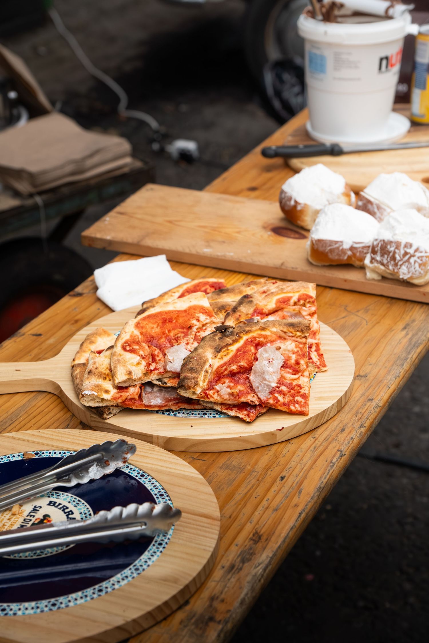 Freshly made pizza slices on a wooden board at an outdoor food stall.