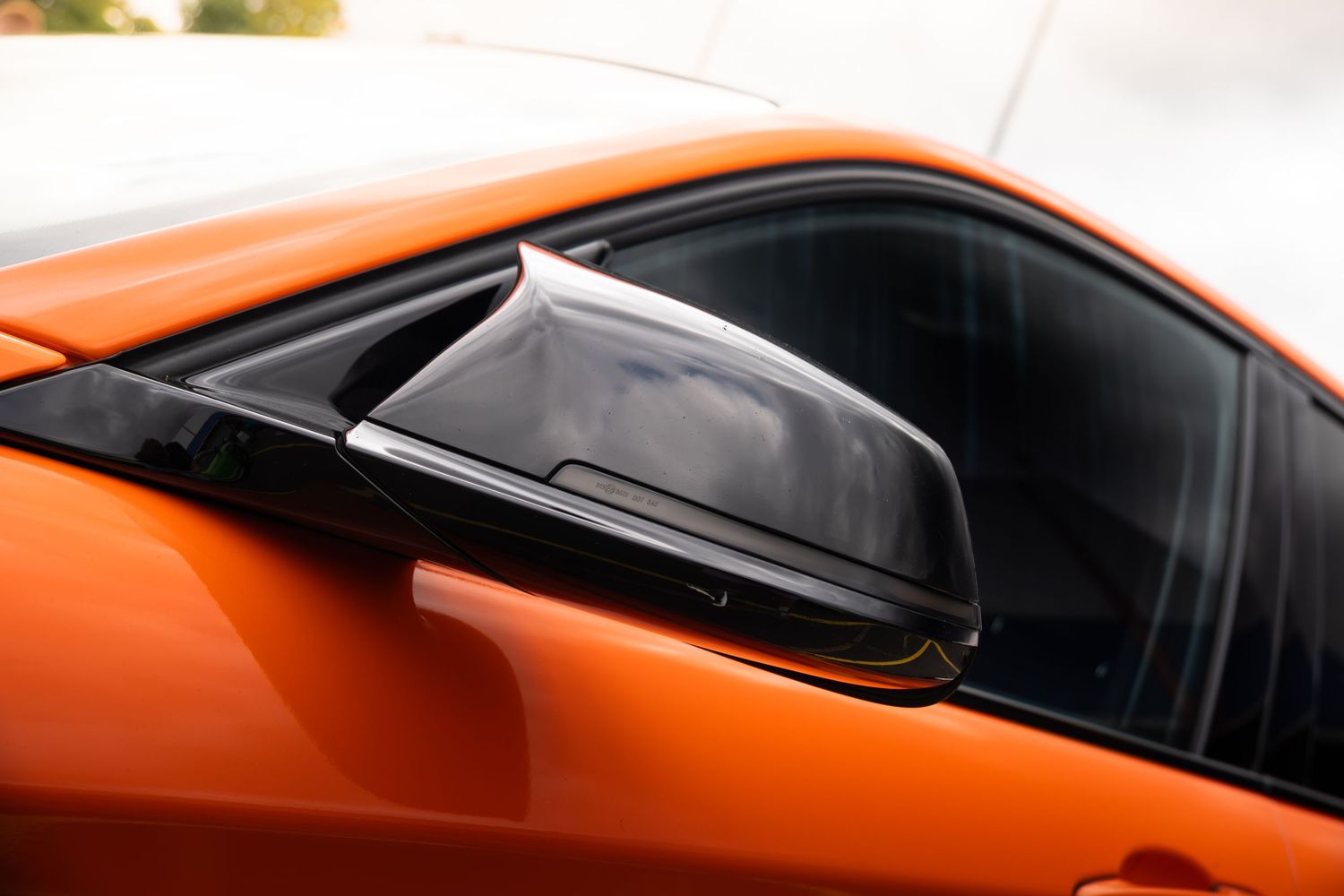 Close-up of a carbon fiber wing mirror on a vibrant orange sports car with tinted windows.