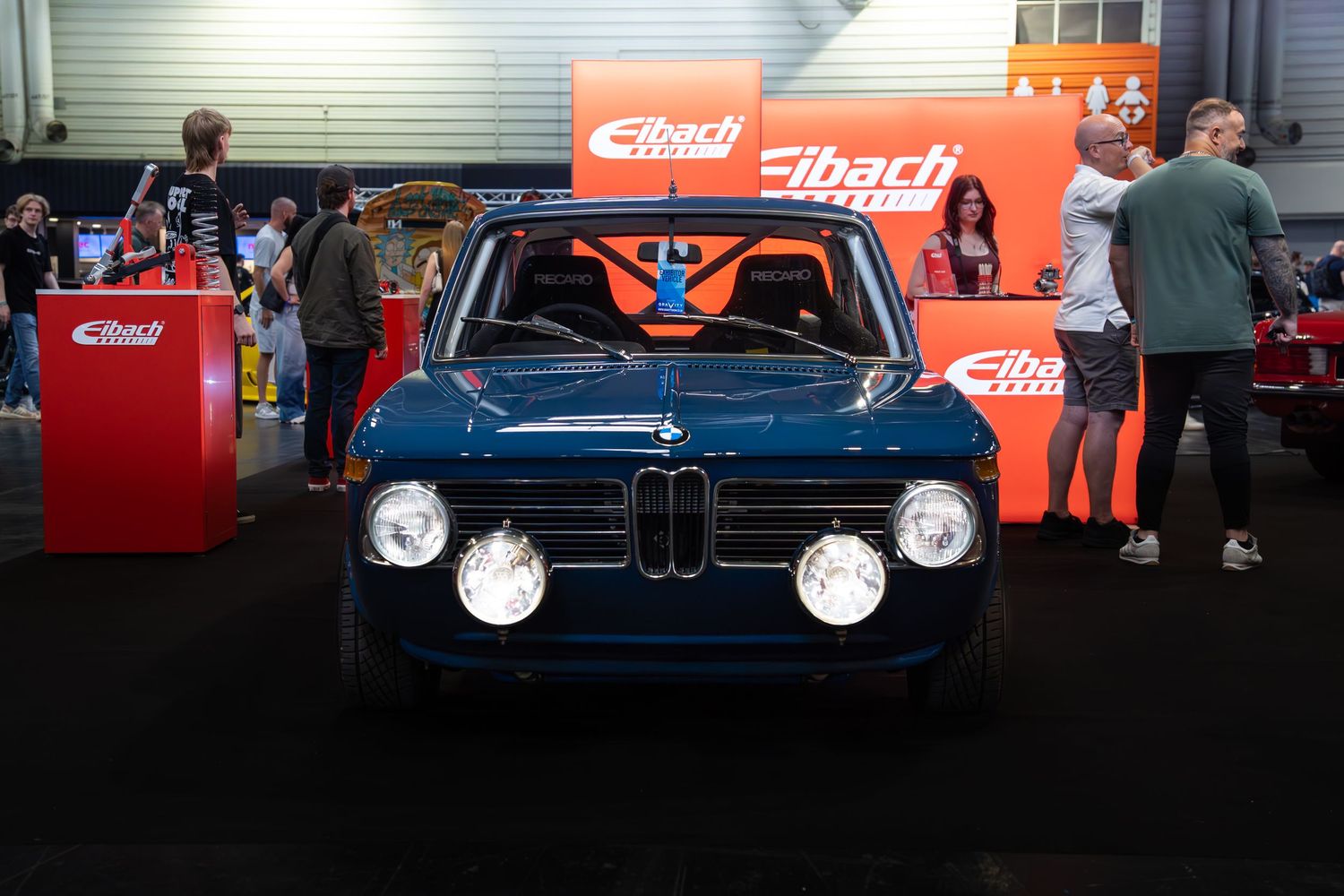 A classic blue BMW 2002 on display at an Eibach Springs automotive exhibition booth.