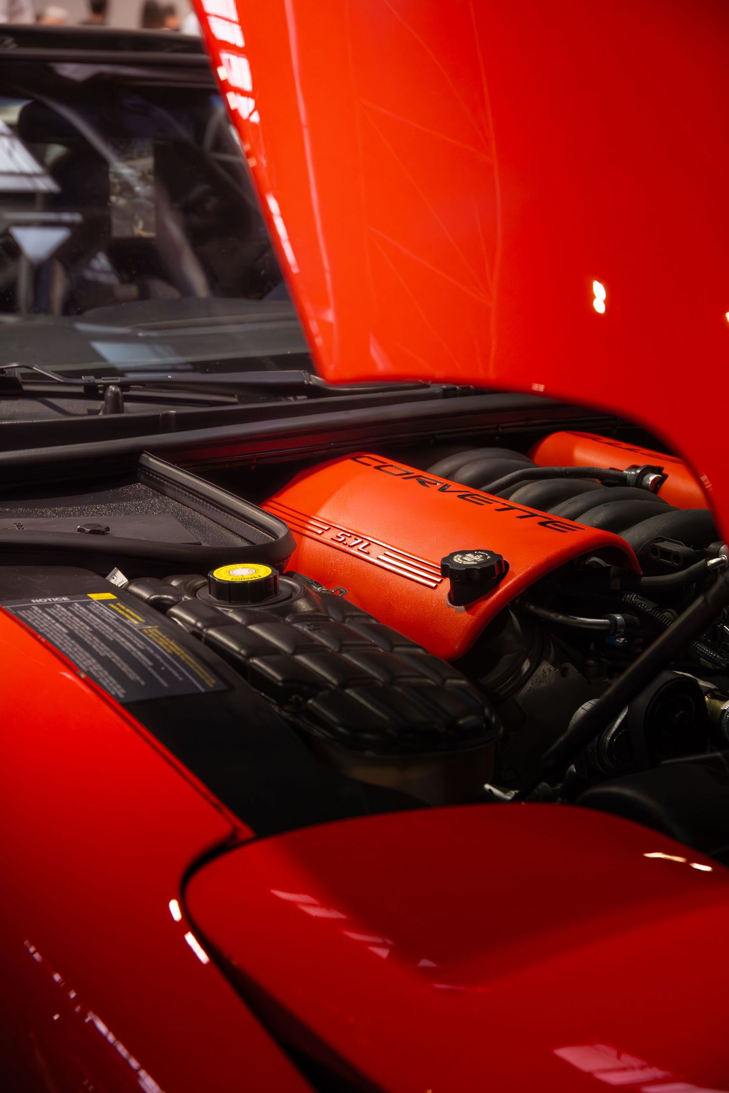 Red Corvette engine bay with orange valve cover on display at a car show.