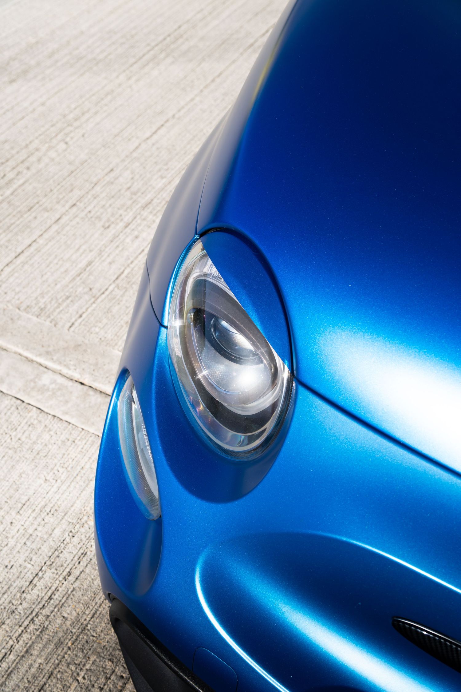 Close-up of the round headlight on a glossy blue Abarth 500 showing sleek bodywork curves.