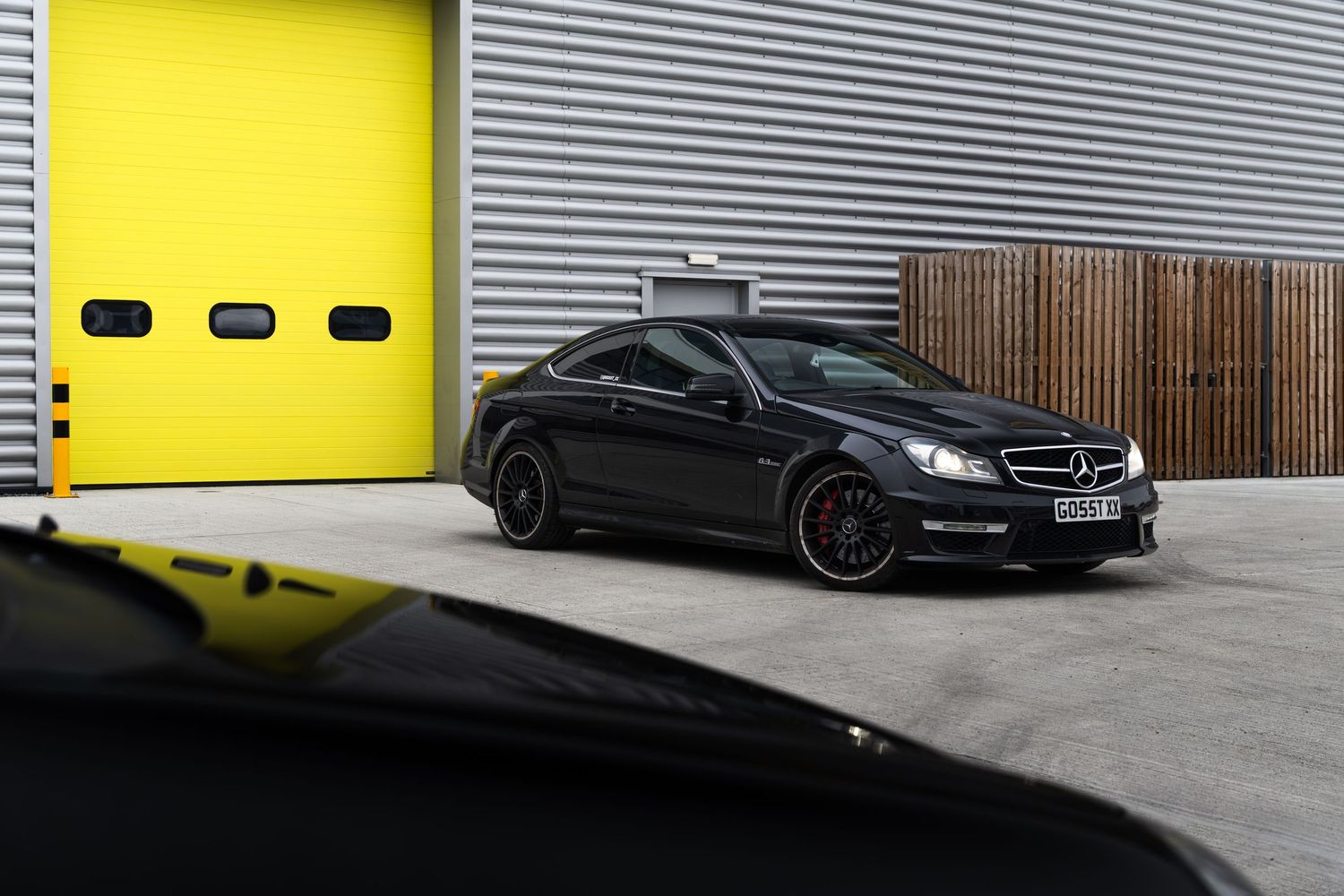 Black Mercedes-AMG C63 coupe parked outside a garage with yellow doors.