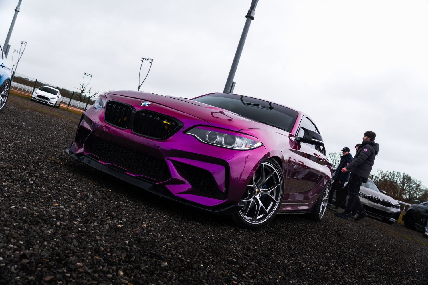 Purple widebody BMW M2 with aggressive styling at an outdoor car meet event.