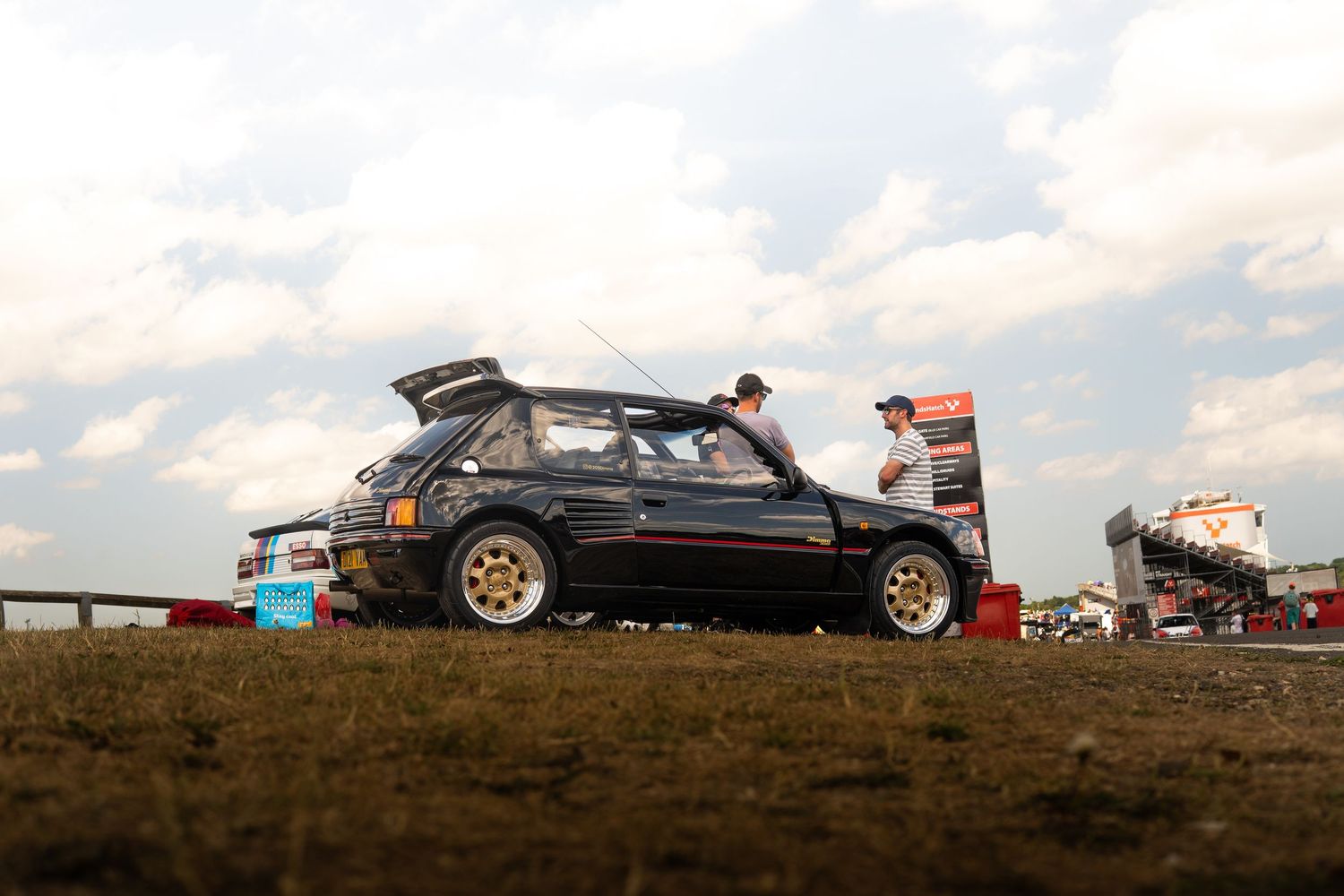 Black Peugeot 205 T16 rally car parked on grass at motorsport event.