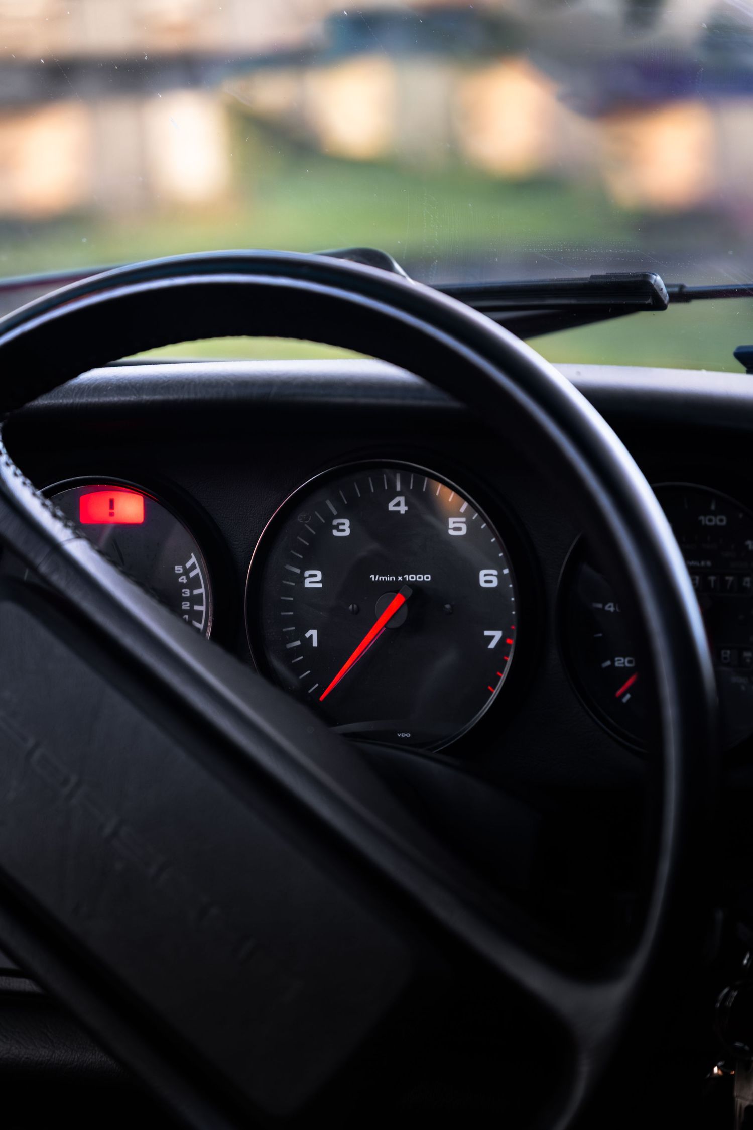 Interior view of a Porsche 911 dashboard showing tachometer through the steering wheel in low evening light.