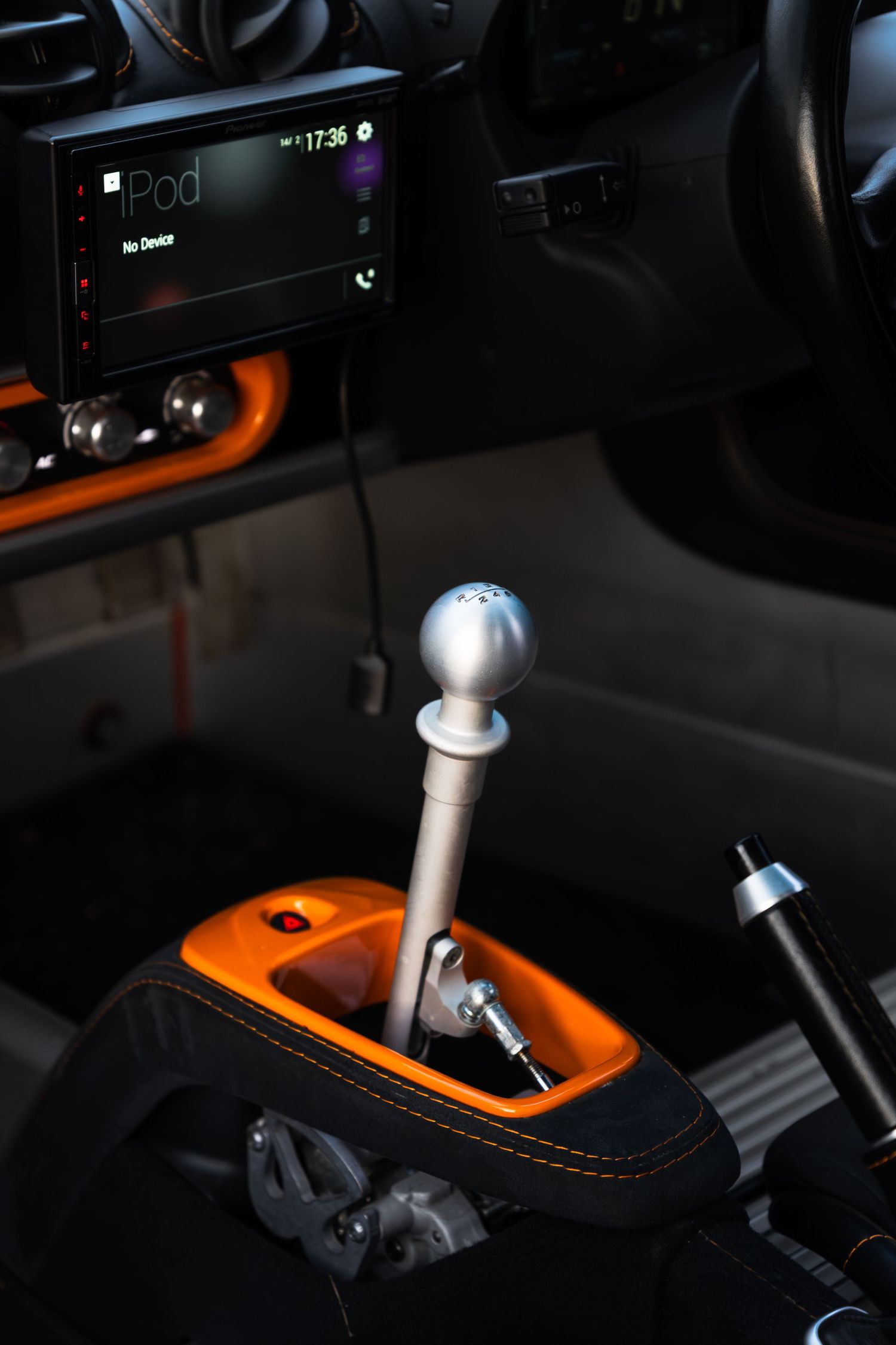 Interior shot of Lotus Elise gear shifter with orange trim surround and Pioneer infotainment screen.