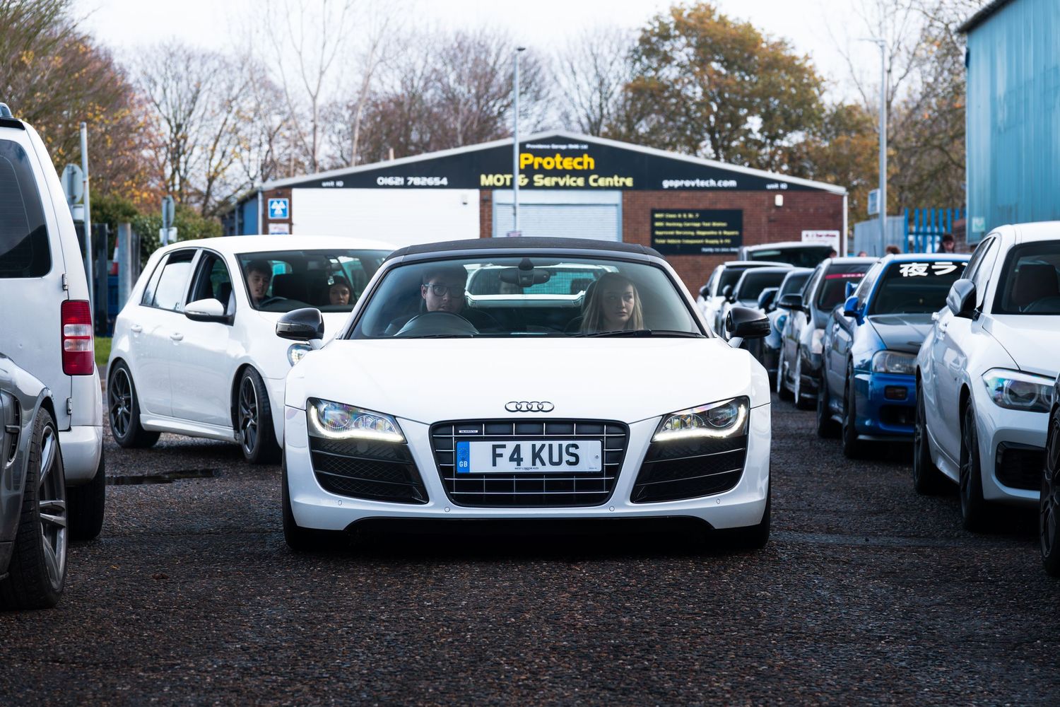 White Audi R8 with plate F4KUS parked at Protech MOT Service Centre surrounded by performance cars.