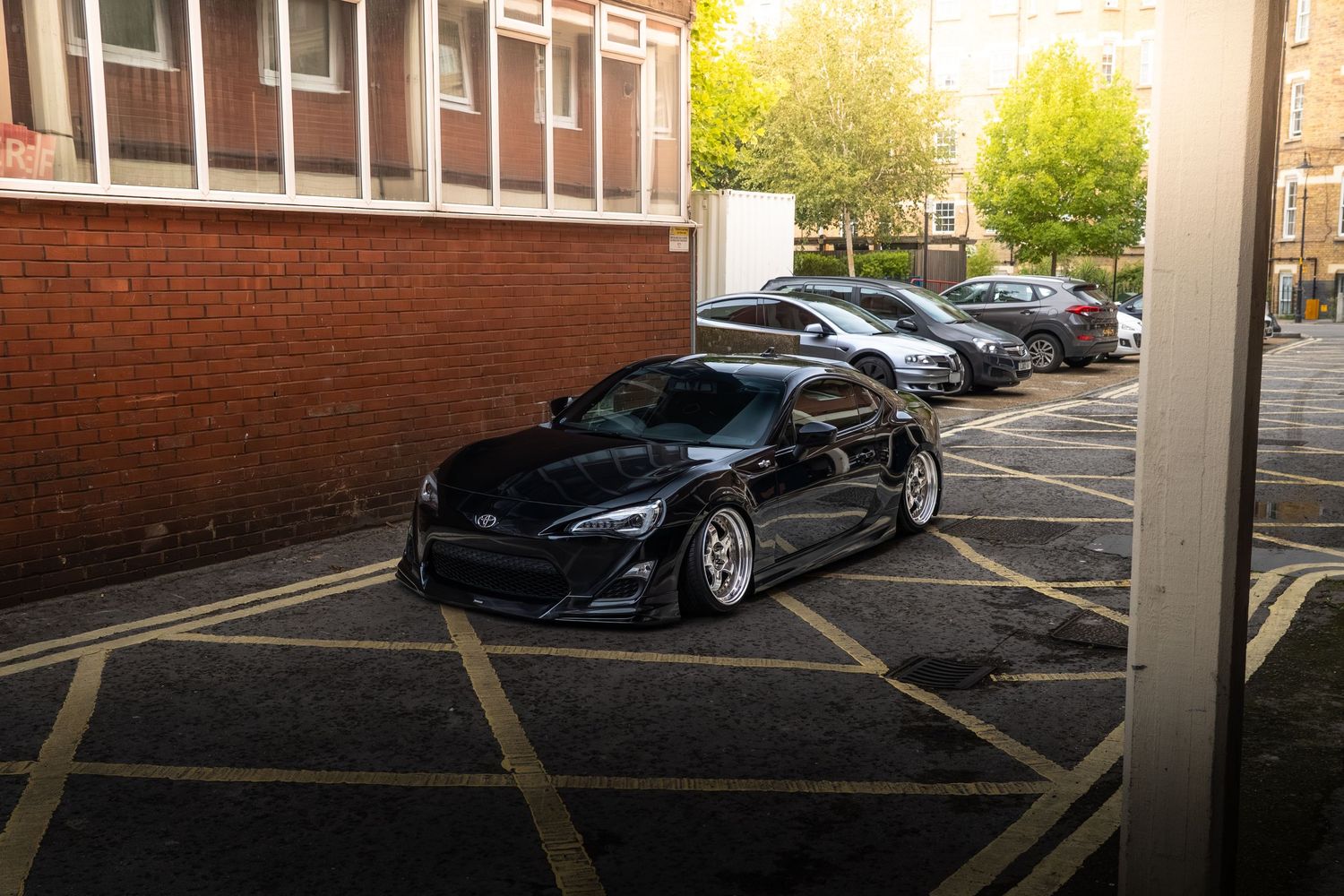 Lowered black Toyota GT86 sports coupe parked in a brick building car park.