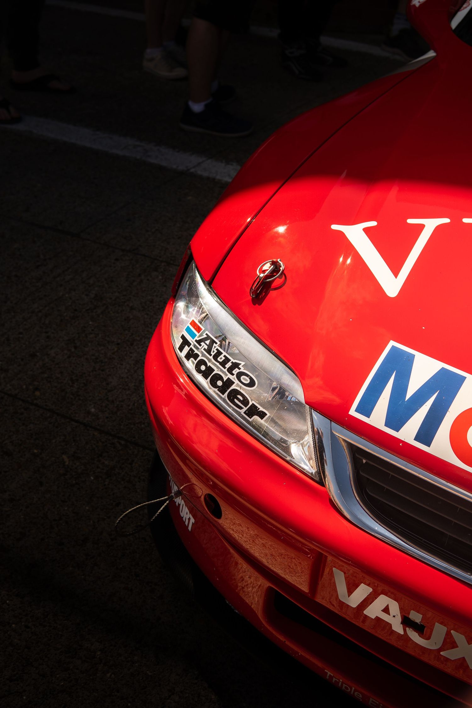 Close-up of red BTCC racing car front with AutoTrader and Mobil 1 sponsor decals in pit lane.