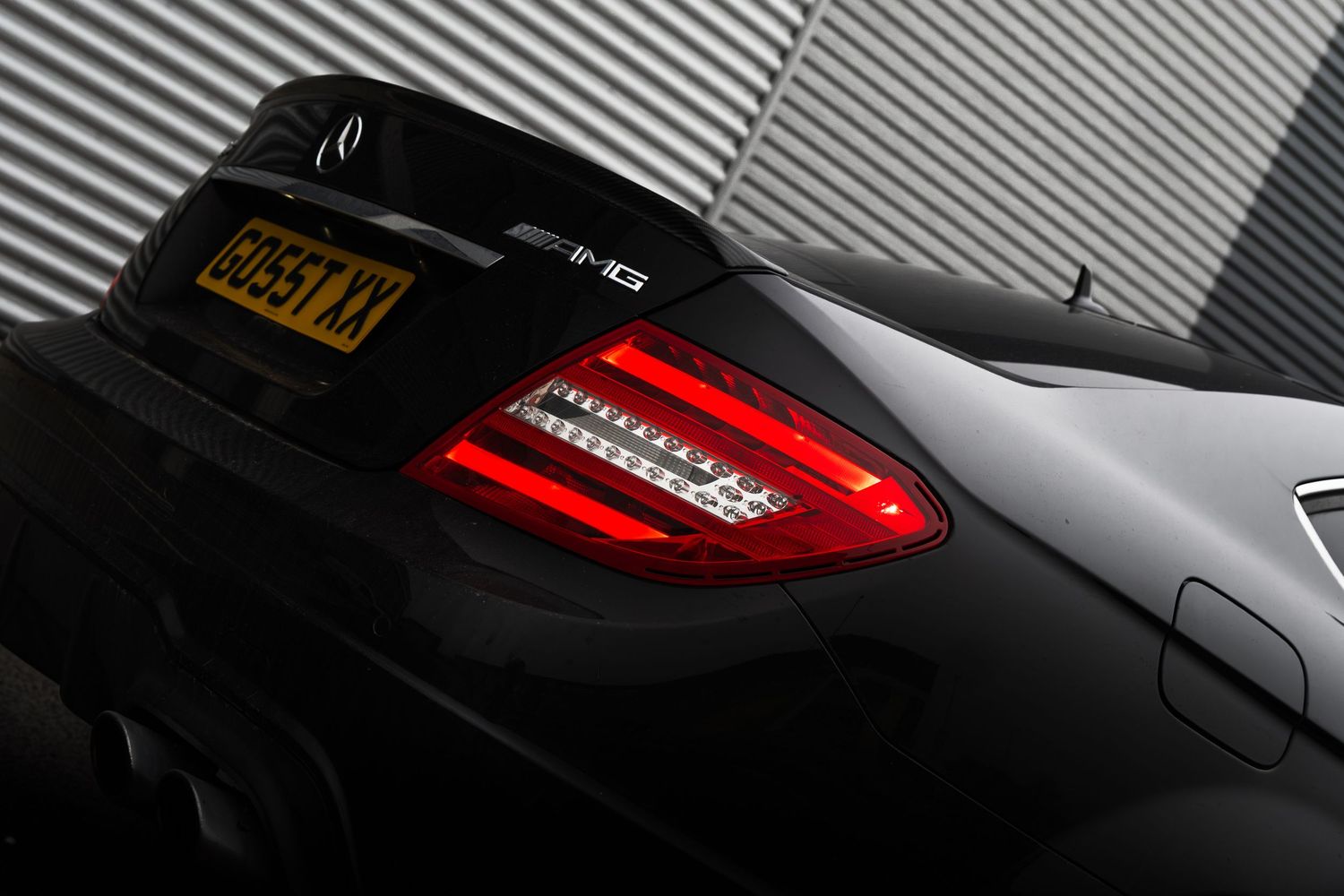 Close-up of black Mercedes-AMG C63 rear LED taillights and trunk spoiler with UK license plate.